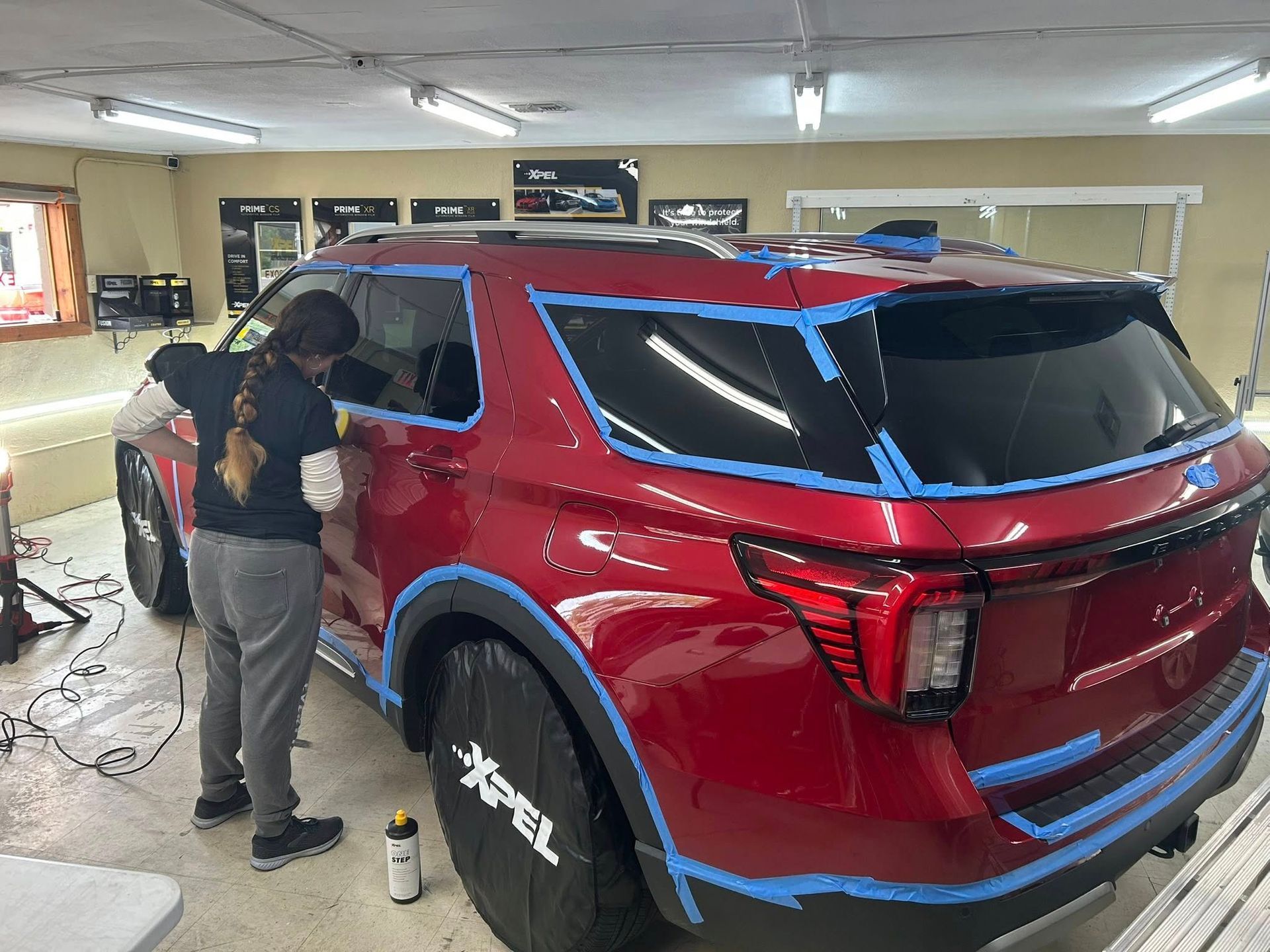 A person working on a red SUV inside a garage, applying a protective film, with blue tape outlining the edges.