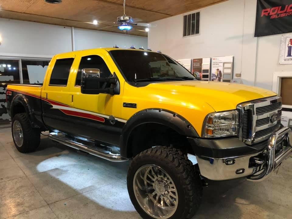 Yellow Ford truck with black and red accents, chrome details, lifted, indoors.
