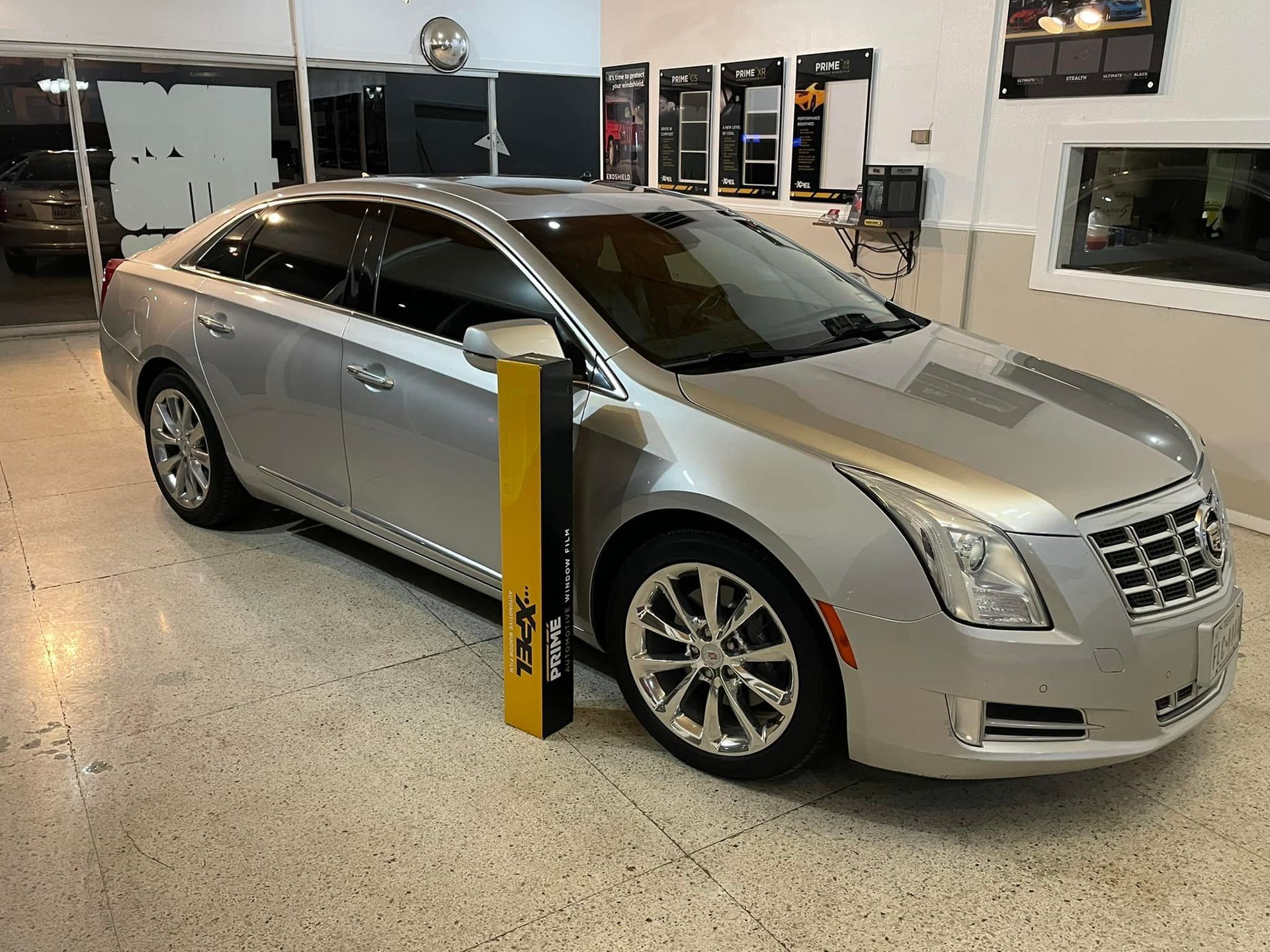 Silver Cadillac XTS sedan in a shop with window tinting materials.