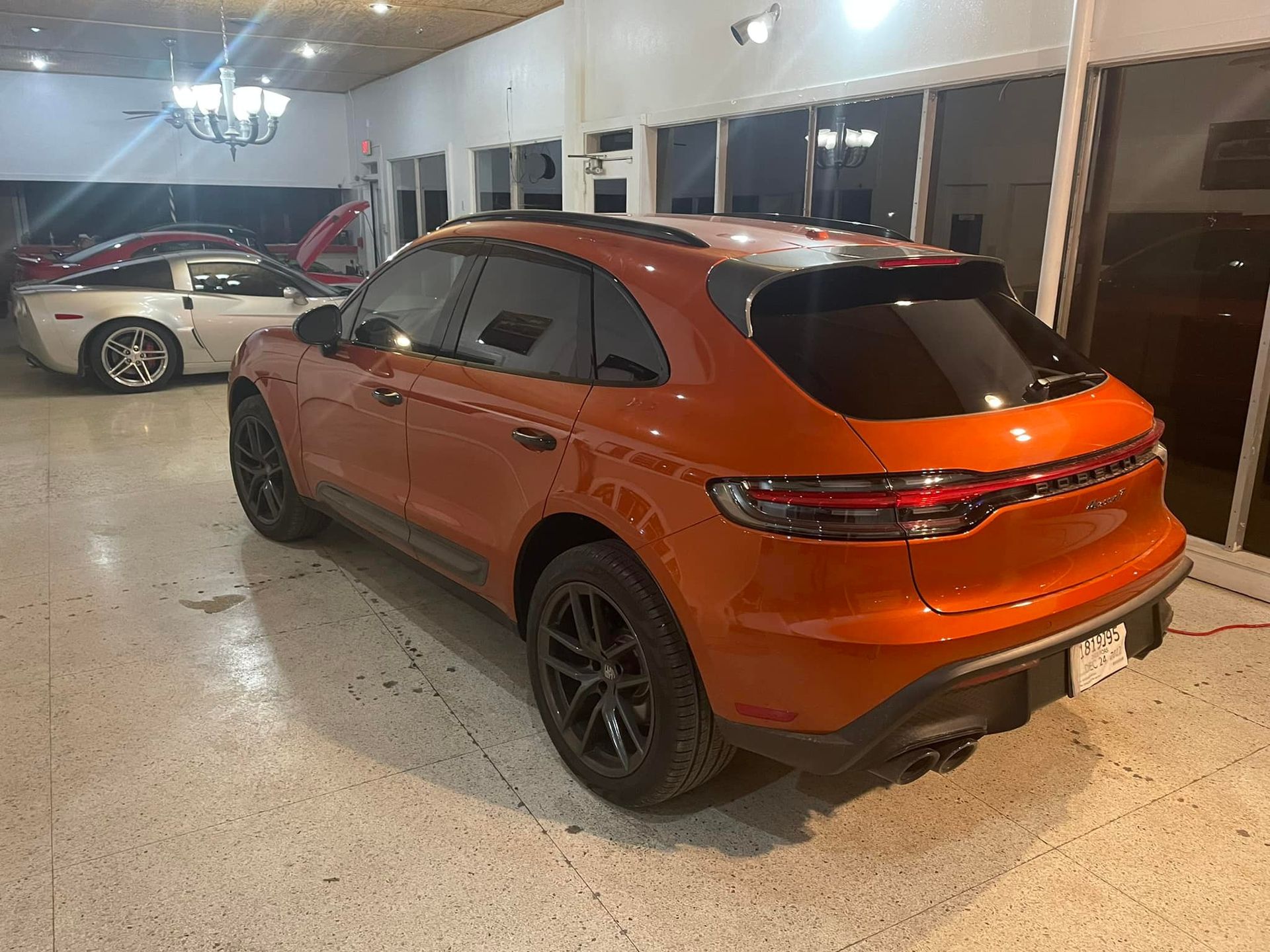 Orange Porsche Macan SUV in a showroom with a silver Corvette.