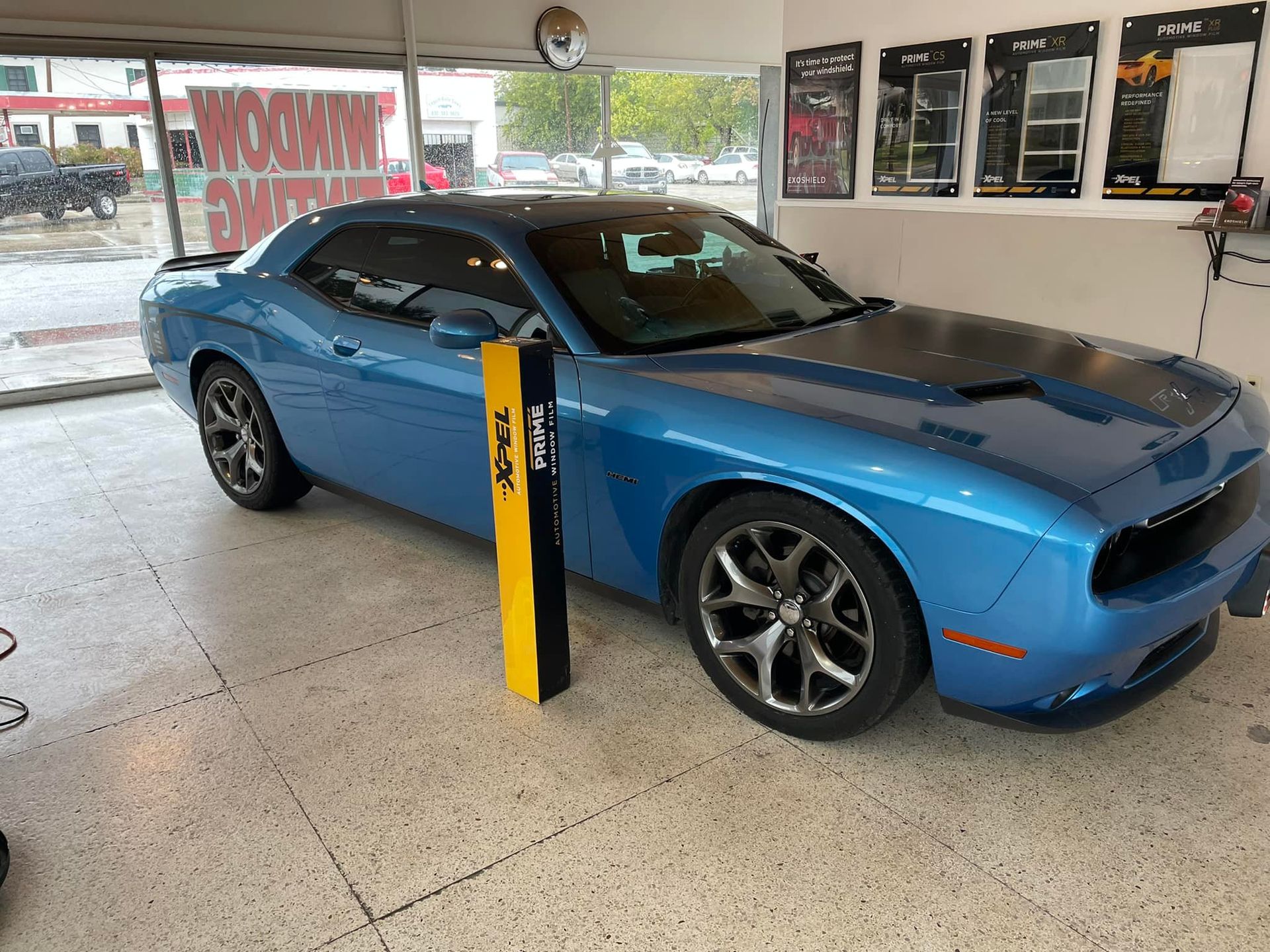 Blue Dodge Challenger car inside a shop, standing next to yellow and black package.