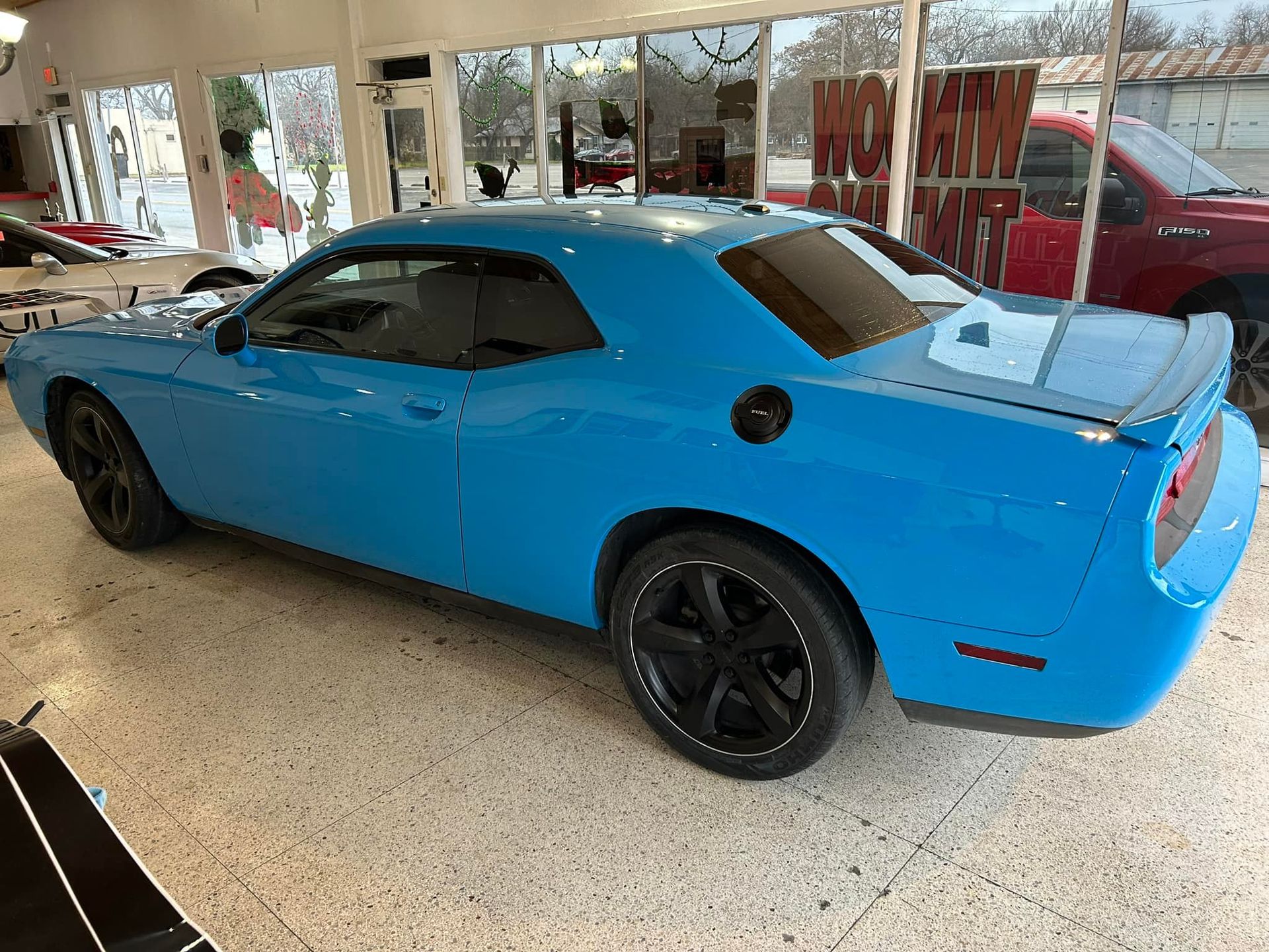 Bright blue Dodge Challenger with black wheels parked inside a showroom.