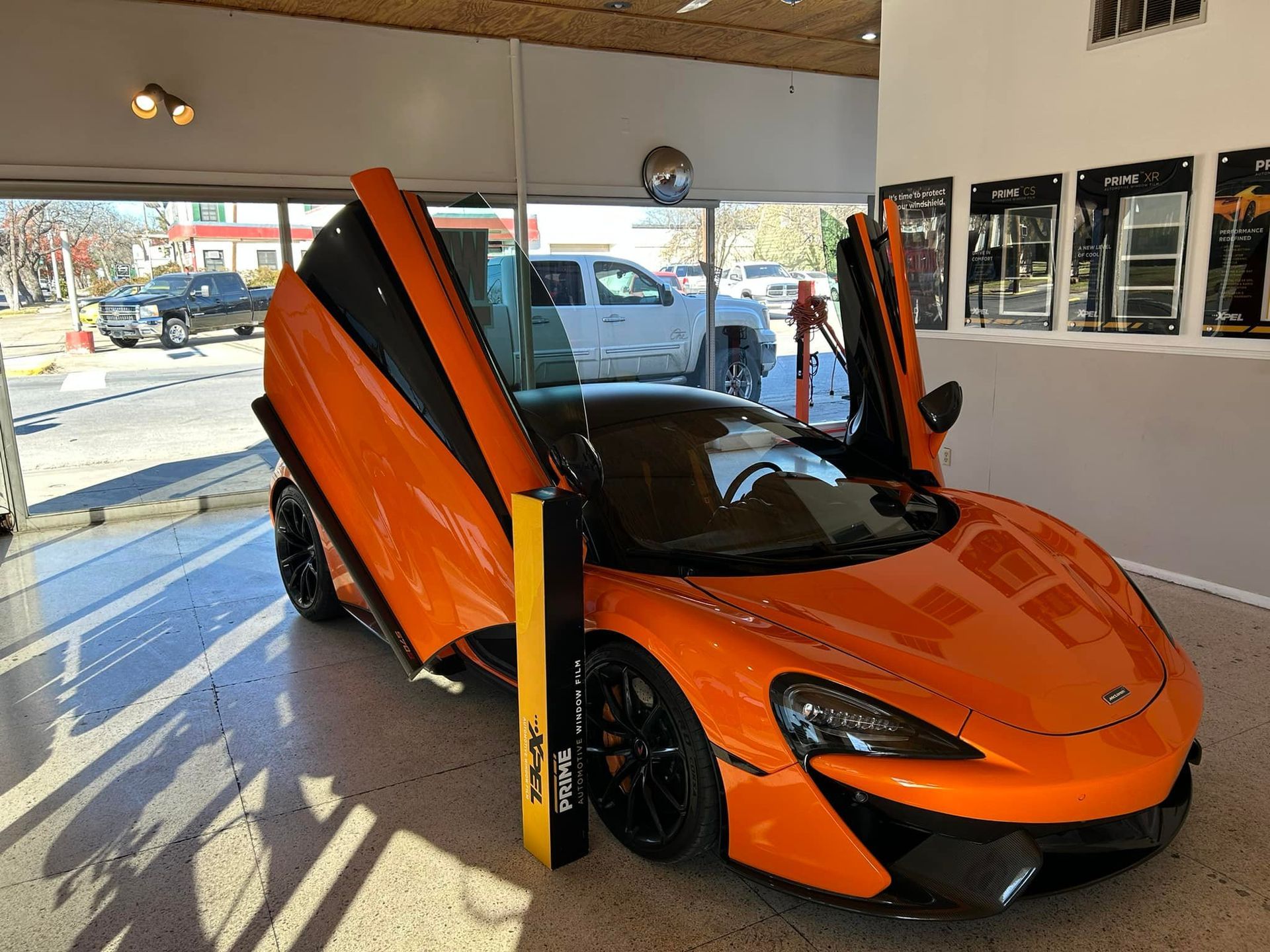 Bright orange McLaren sports car with open doors on display inside a showroom.