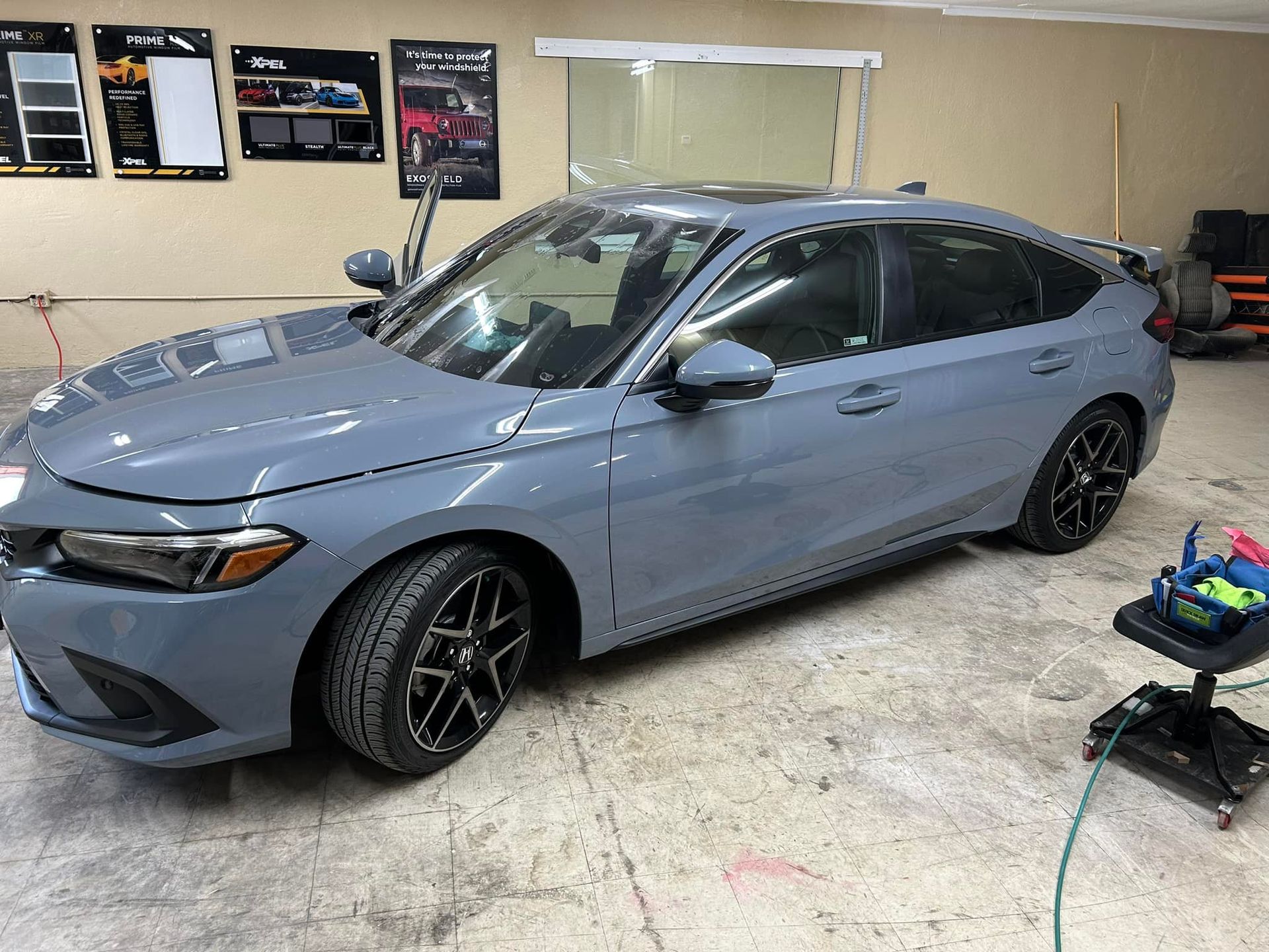 Gray Honda Civic in a garage, door open, black wheels, tinted windows.