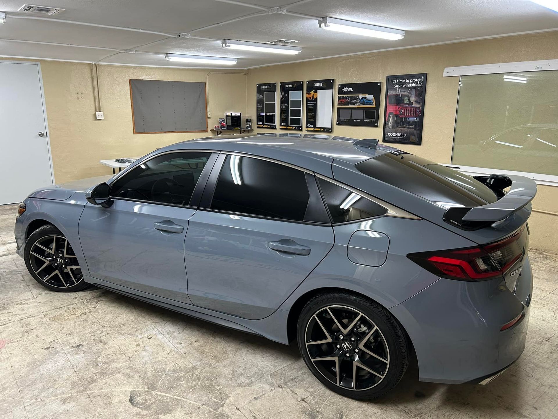 Gray Honda Civic hatchback with tinted windows, black wheels, and a rear spoiler in a garage.