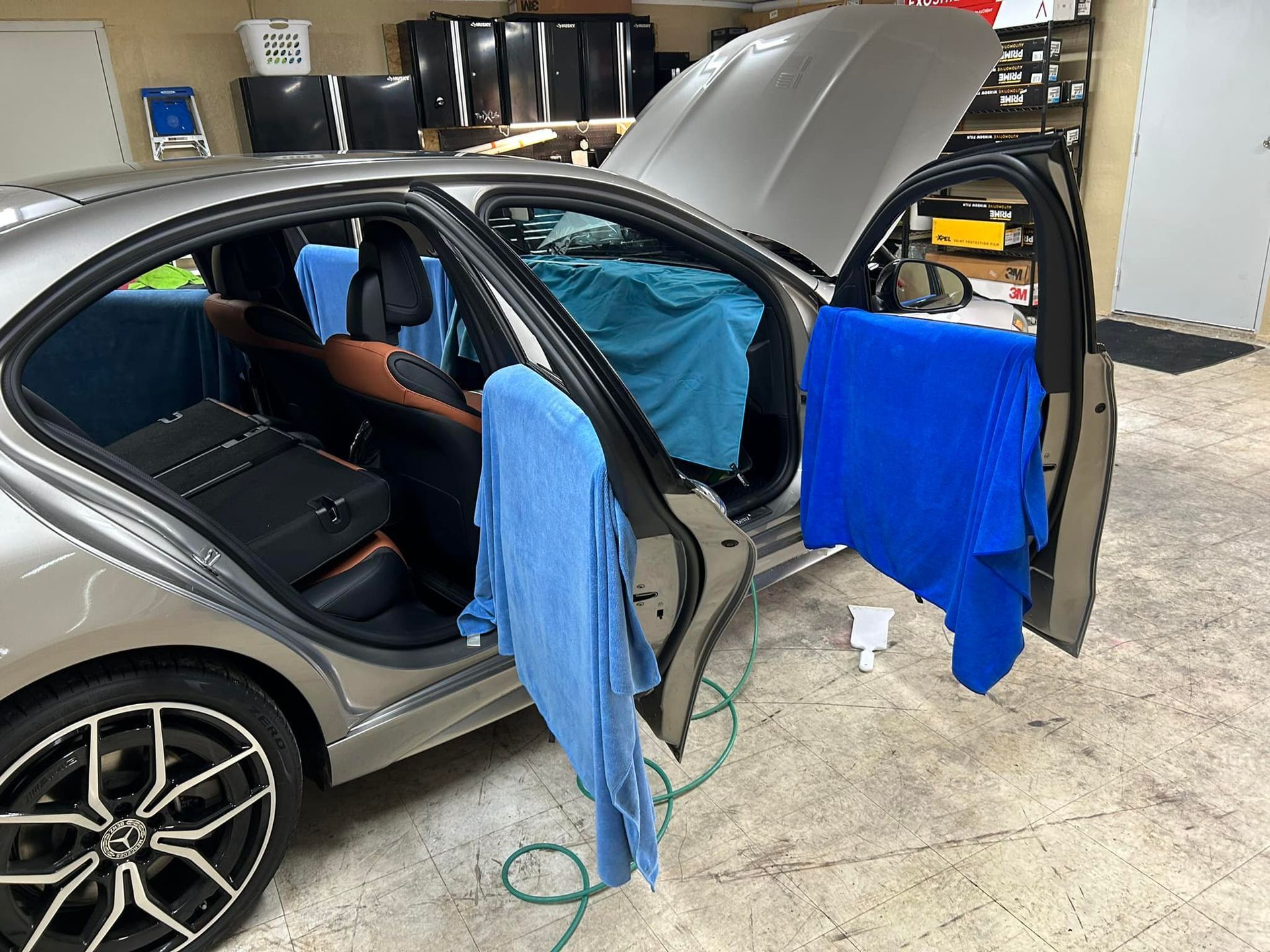 Car with open doors and hood, blue towels hanging. Inside a garage, likely for window tinting.