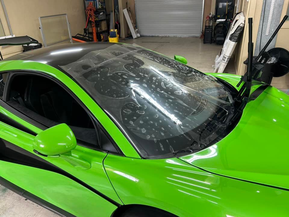 Green sports car with film applied to the windshield, parked inside a garage.