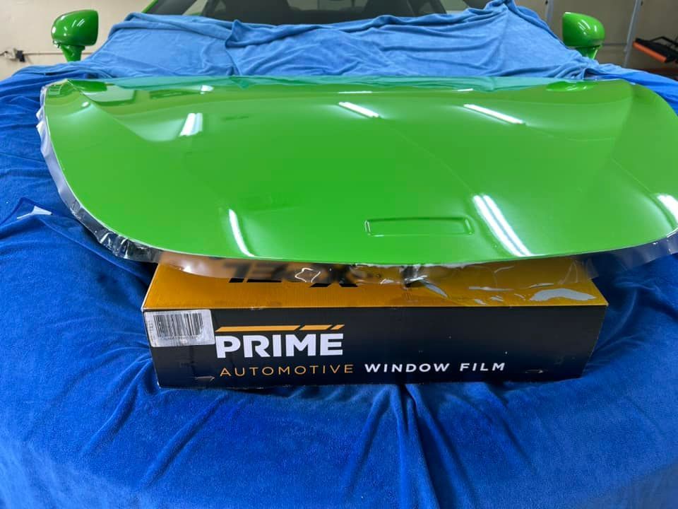 Green car hood on a blue surface, with a box of window film.