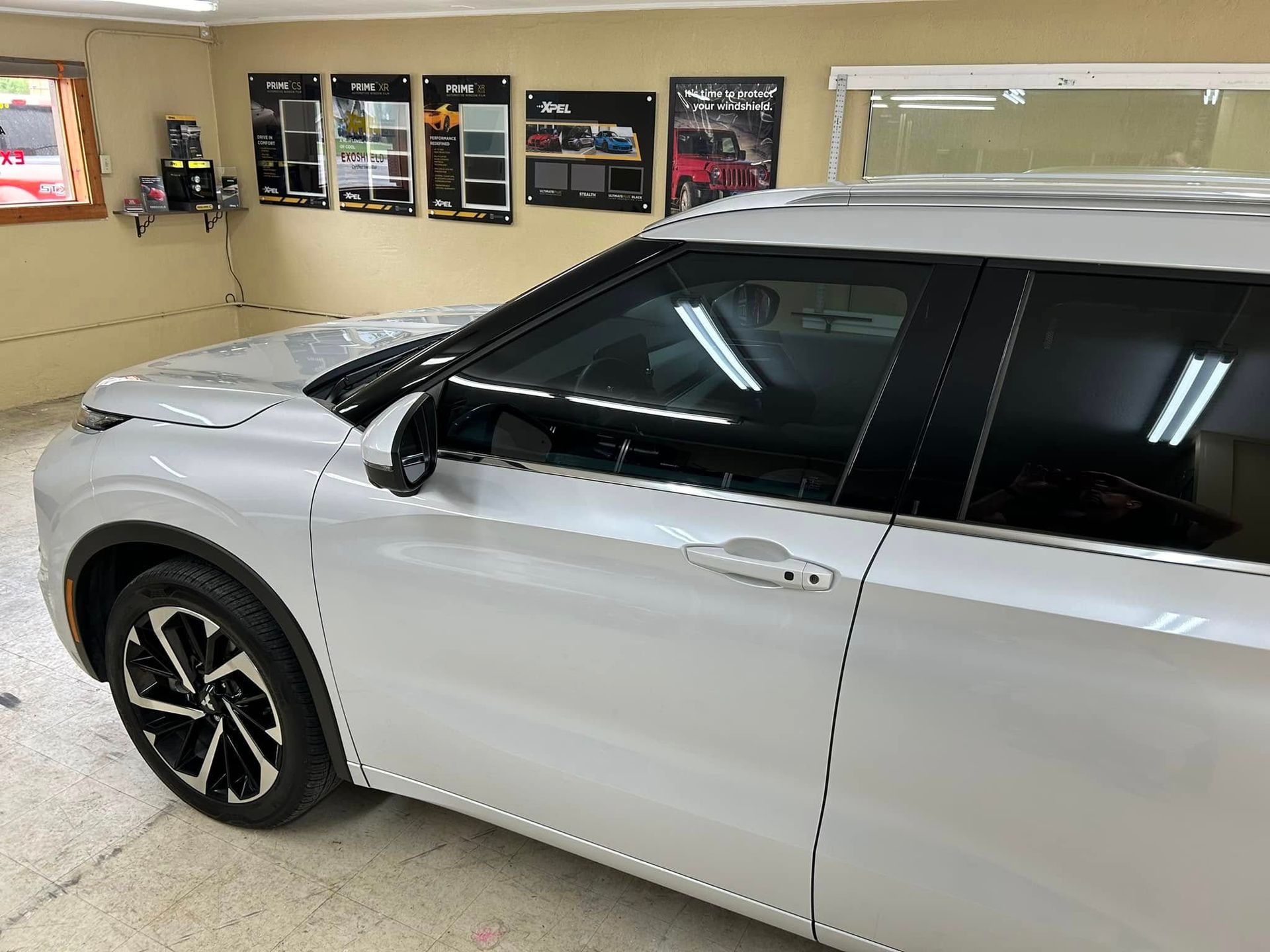 White SUV with tinted windows in a shop; display of tint samples on the wall.