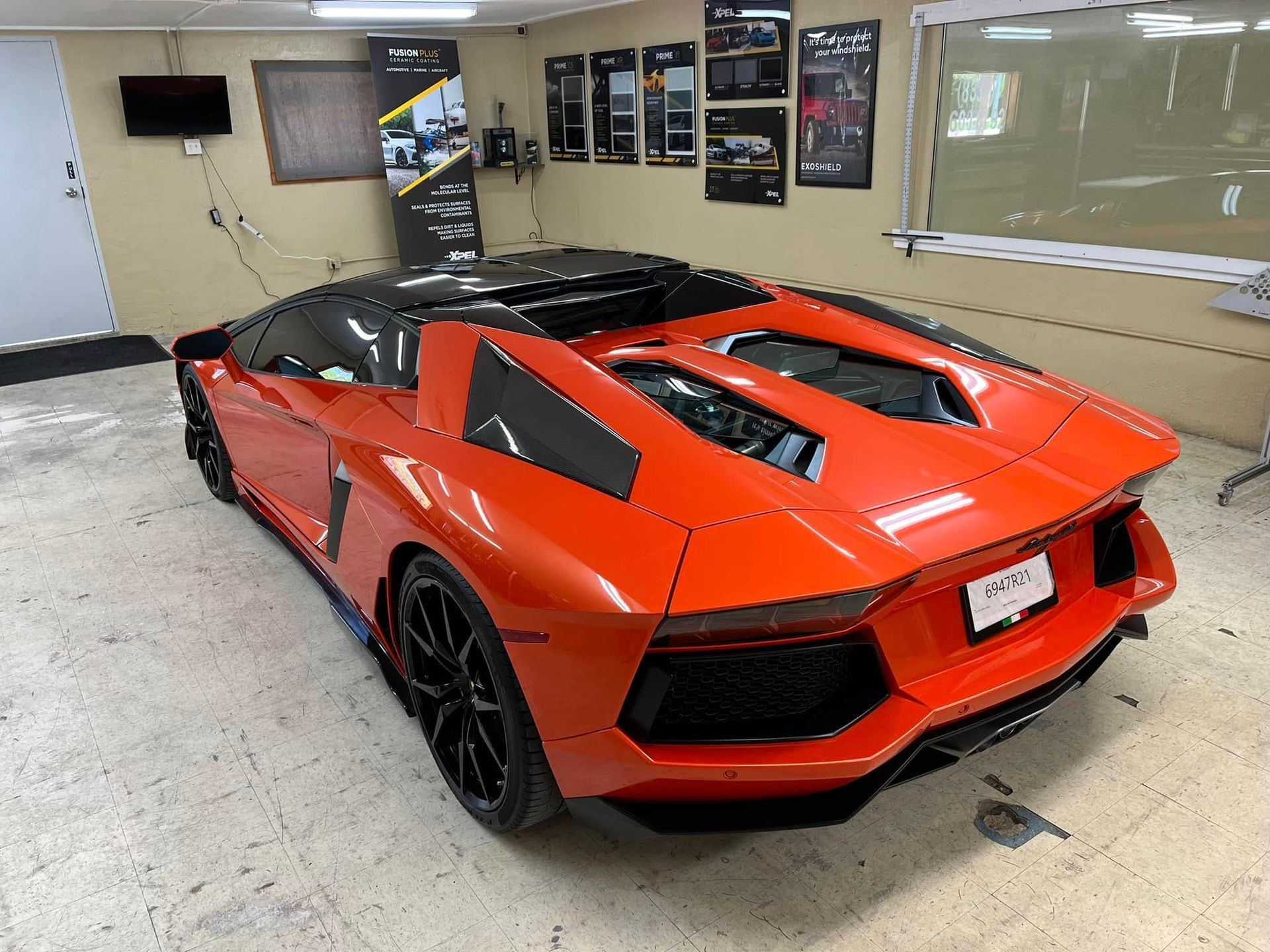 Orange Lamborghini in a garage, black roof and wheels, showroom display.