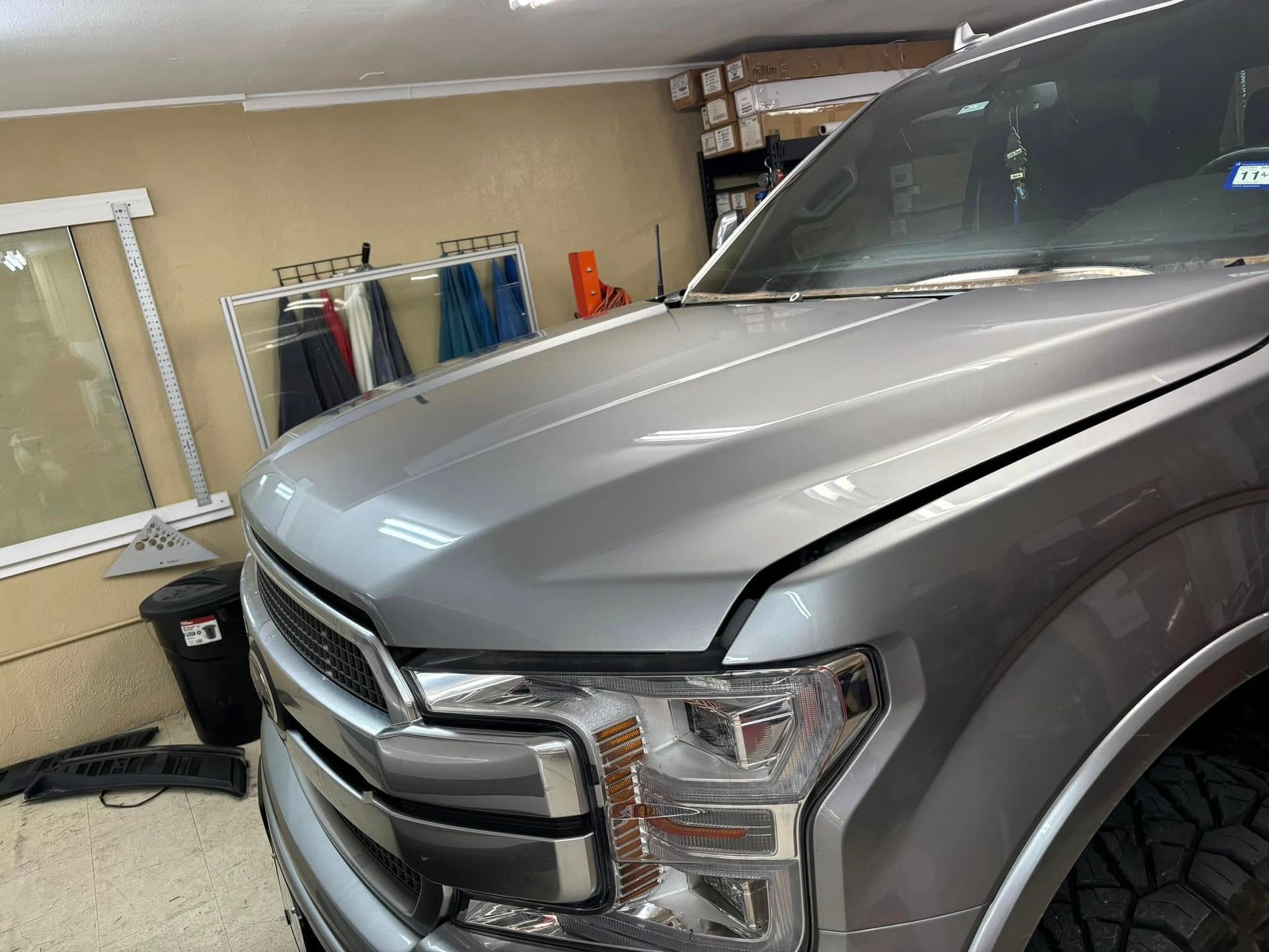 Silver pickup truck hood partially open in a garage.