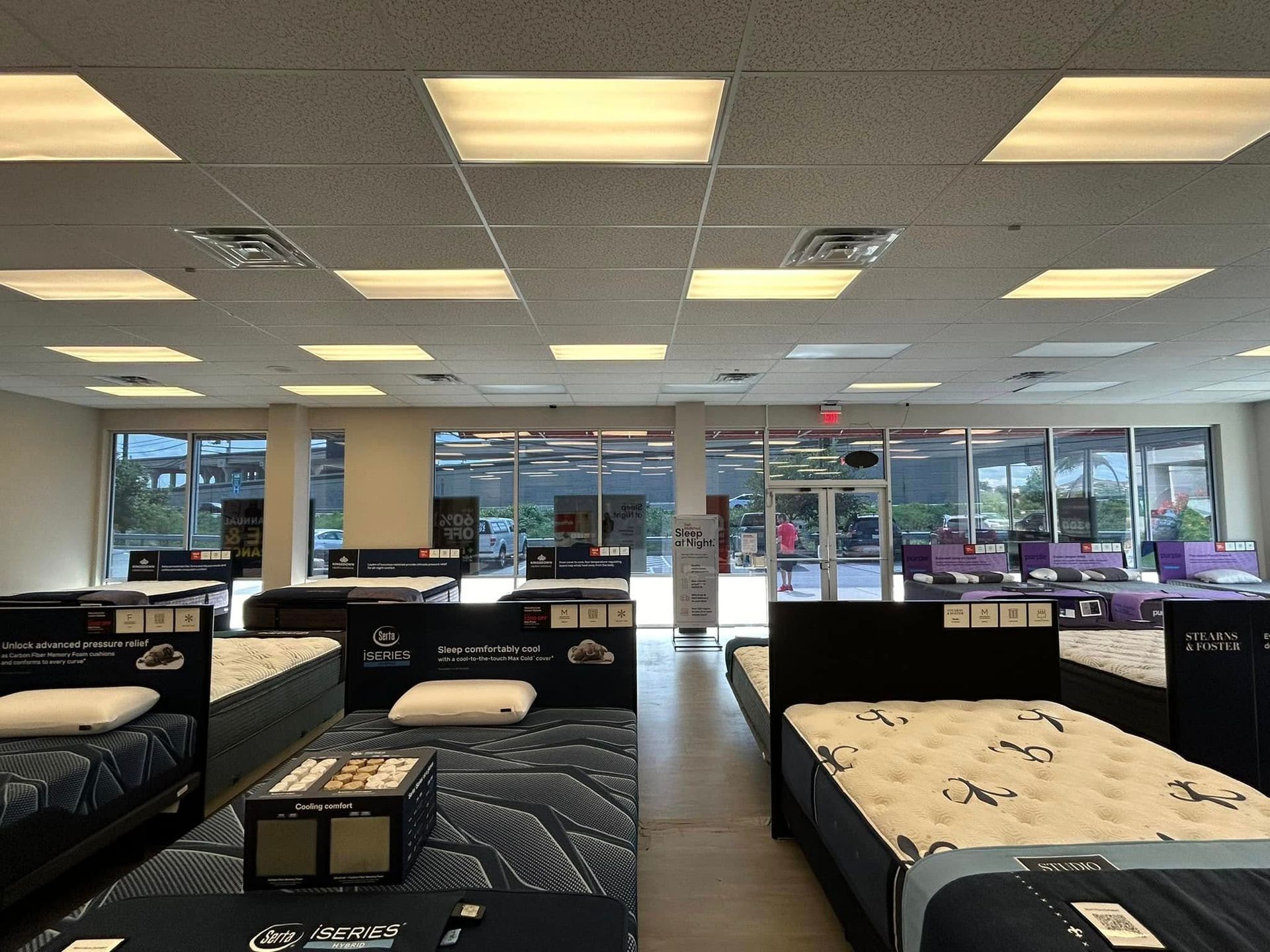 Mattress store interior with rows of beds, fluorescent lights, and large windows.