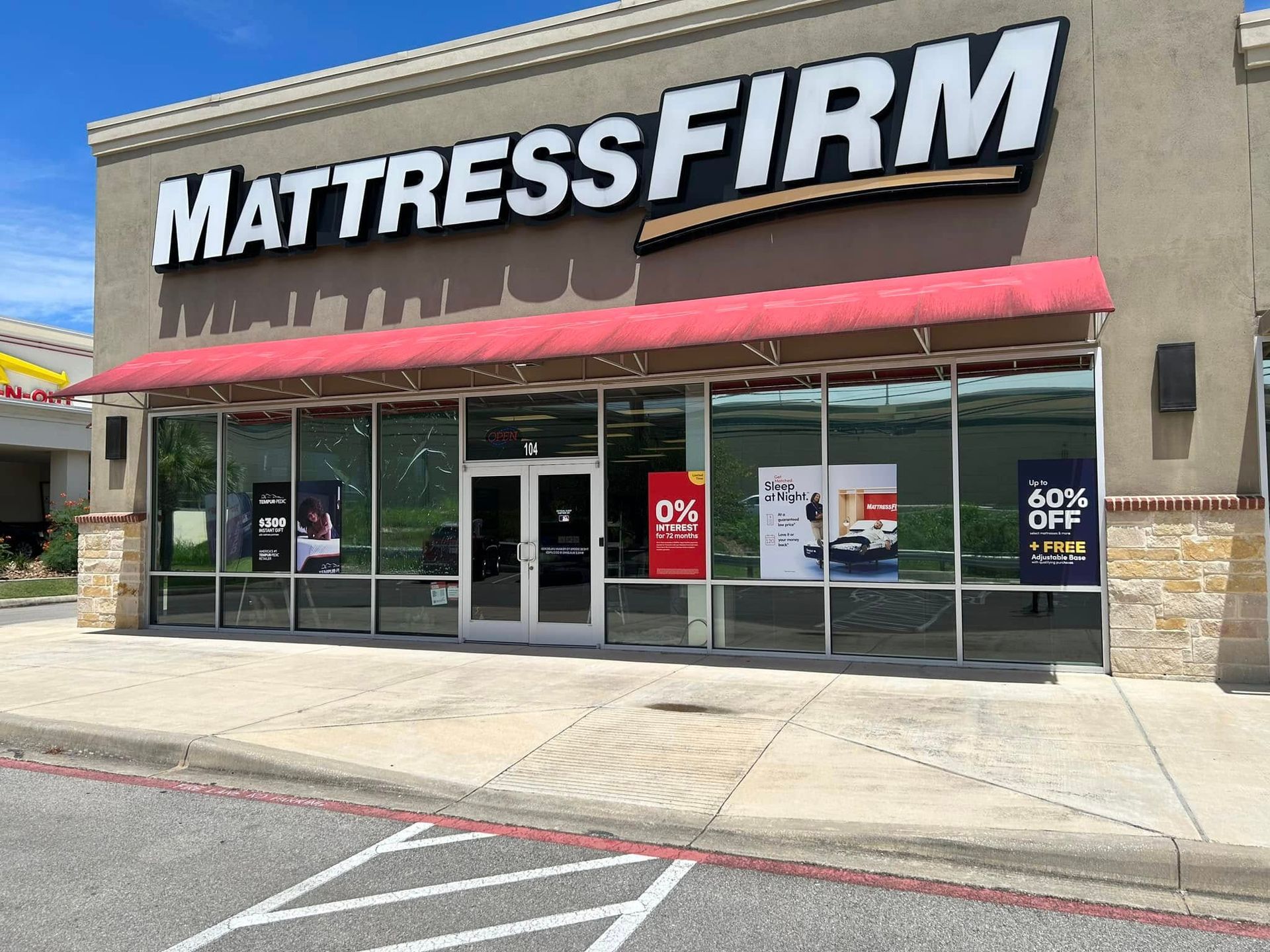 Exterior view of Mattress Firm store with red awning, glass windows, and advertising signs.