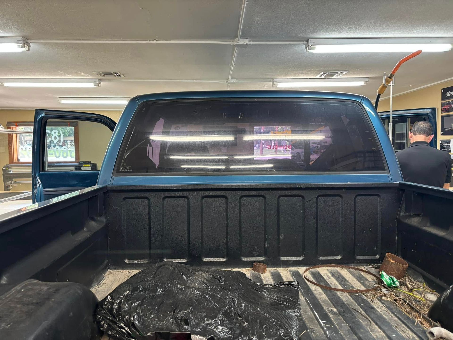 Blue pickup truck bed with a black tarp, a person visible inside a shop.