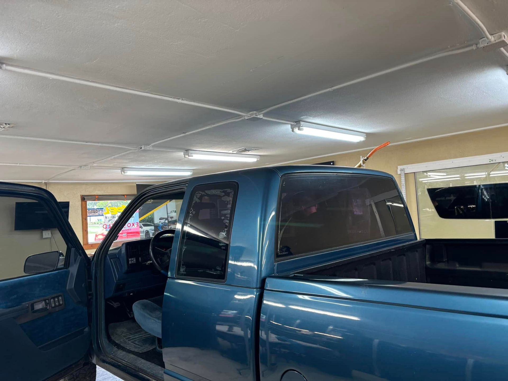 Blue pickup truck with an open door in a well-lit garage.