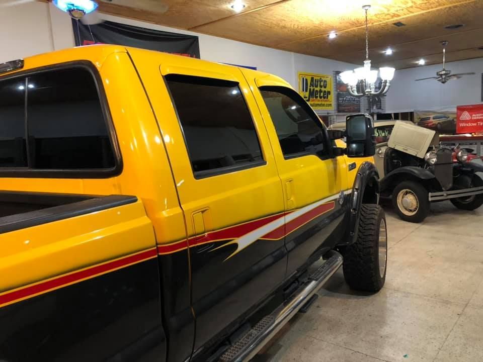 Yellow and black pickup truck, parked in a garage. Classic car in background.