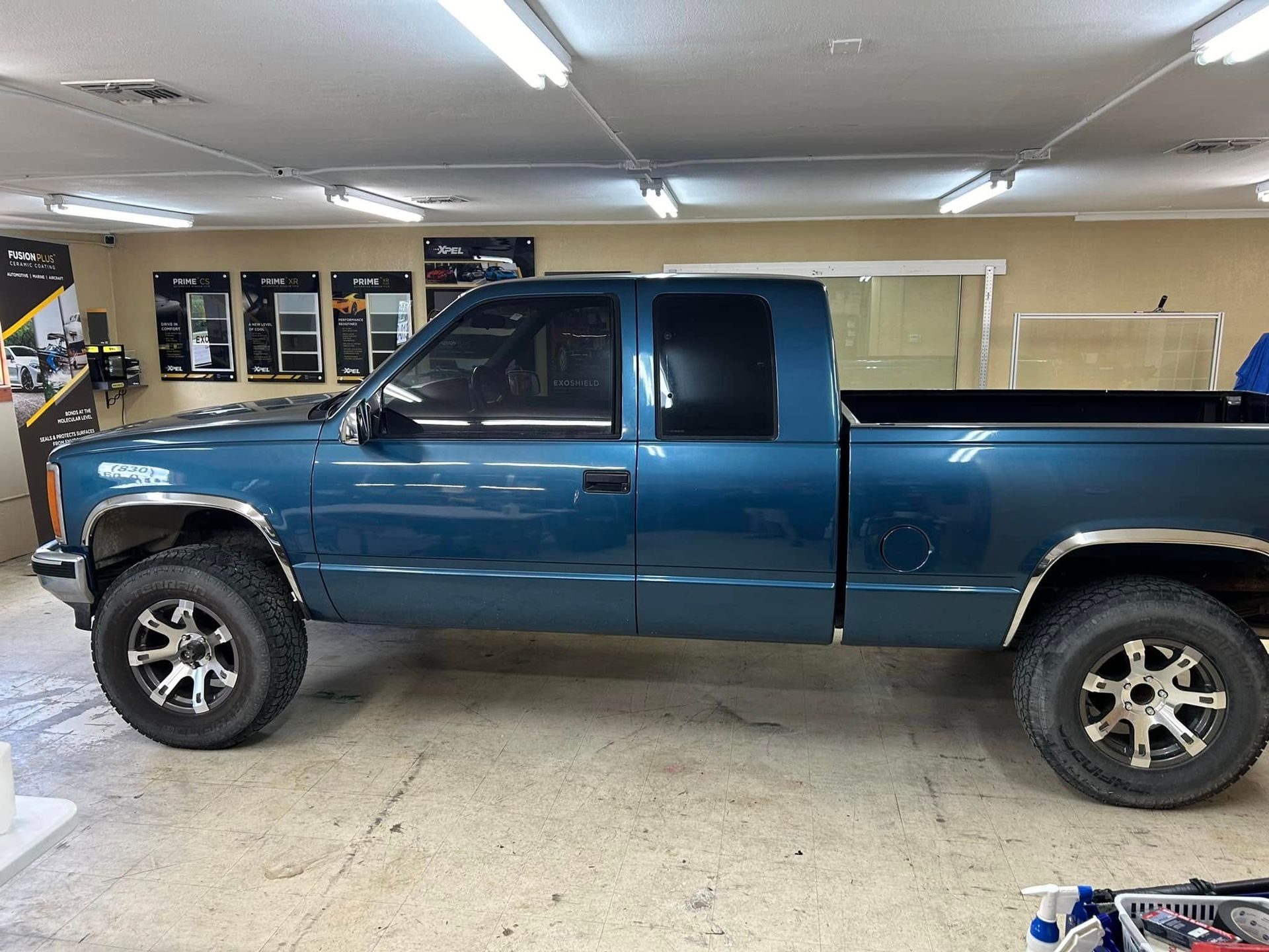 Blue pickup truck with black tinted windows and chrome details inside a shop.