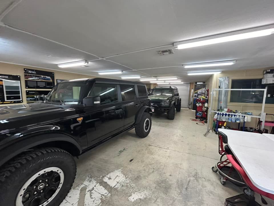 Black and green Ford Broncos inside a garage with tools and work tables.