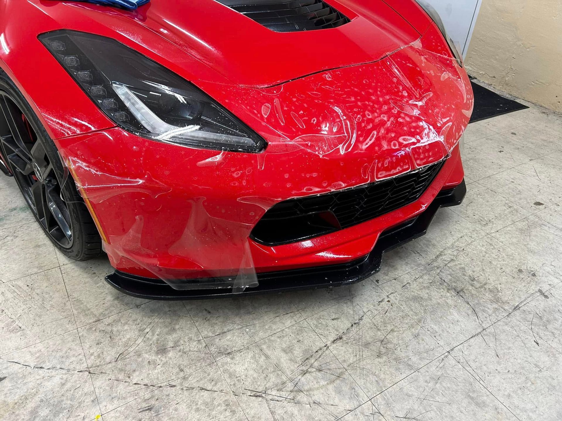 Red sports car with clear protective film on the front bumper.