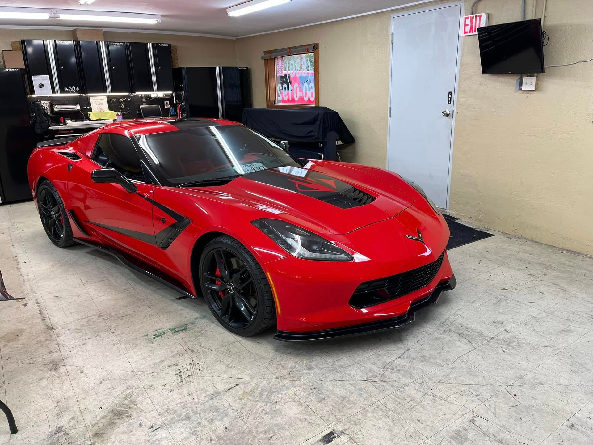Red Corvette sports car parked inside a garage with black cabinets and a door in the background.