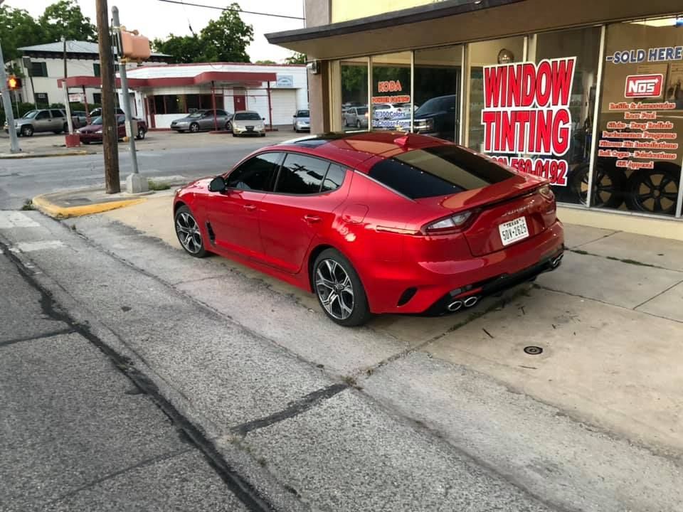 Red Kia Stinger parked outside a window tinting shop on a city street.