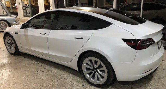 White Tesla Model 3 parked indoors. Black accents, tinted windows, and silver wheels.