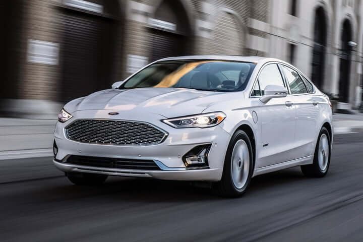 White Ford Fusion Hybrid sedan driving on a city street.