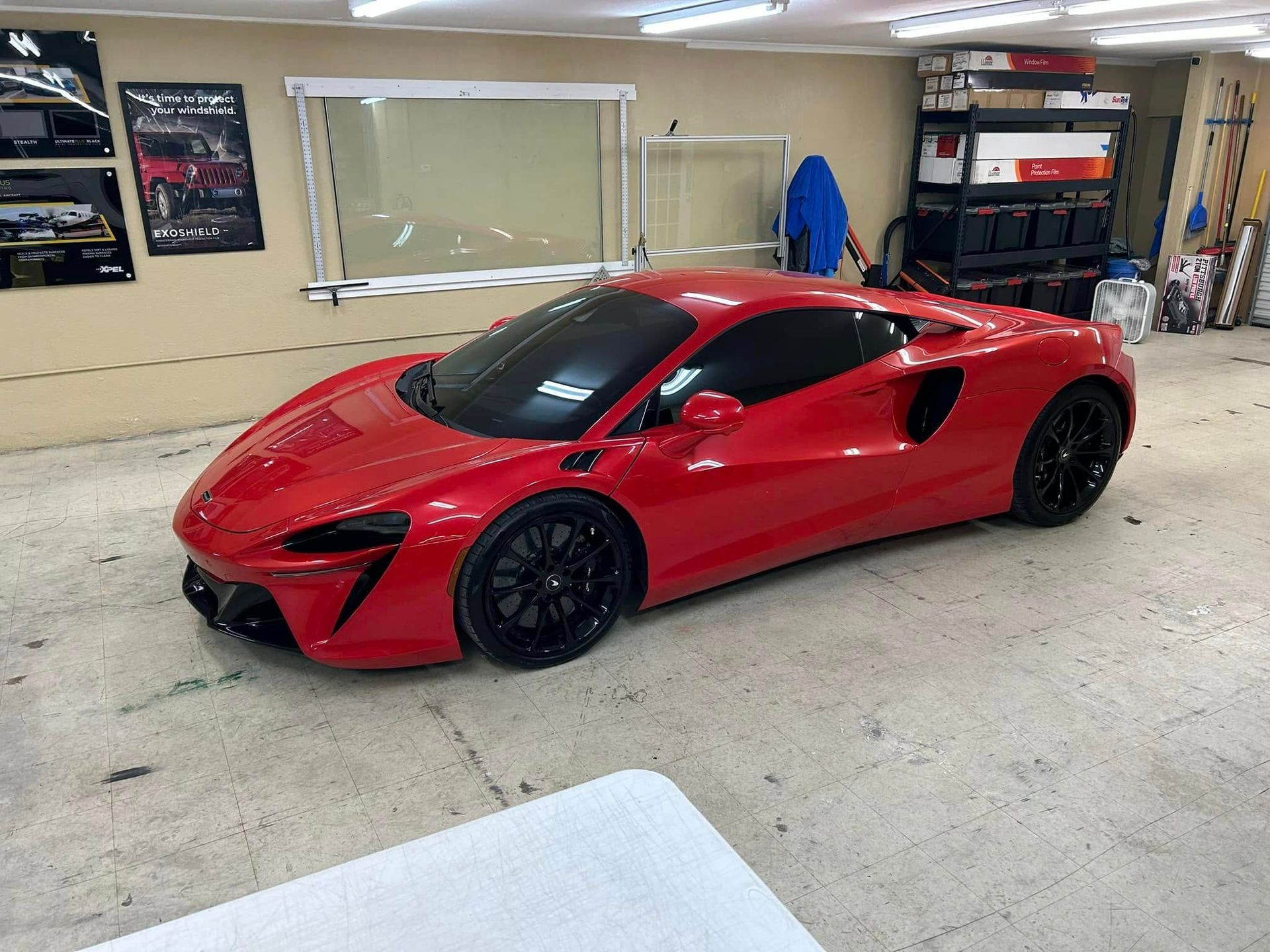 Red McLaren sports car in a garage with black rims and tinted windows.