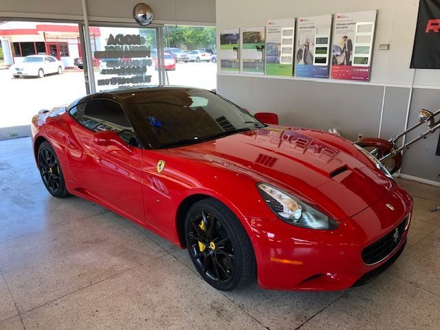 Red Ferrari sports car with black wheels and yellow brake calipers parked inside a shop.
