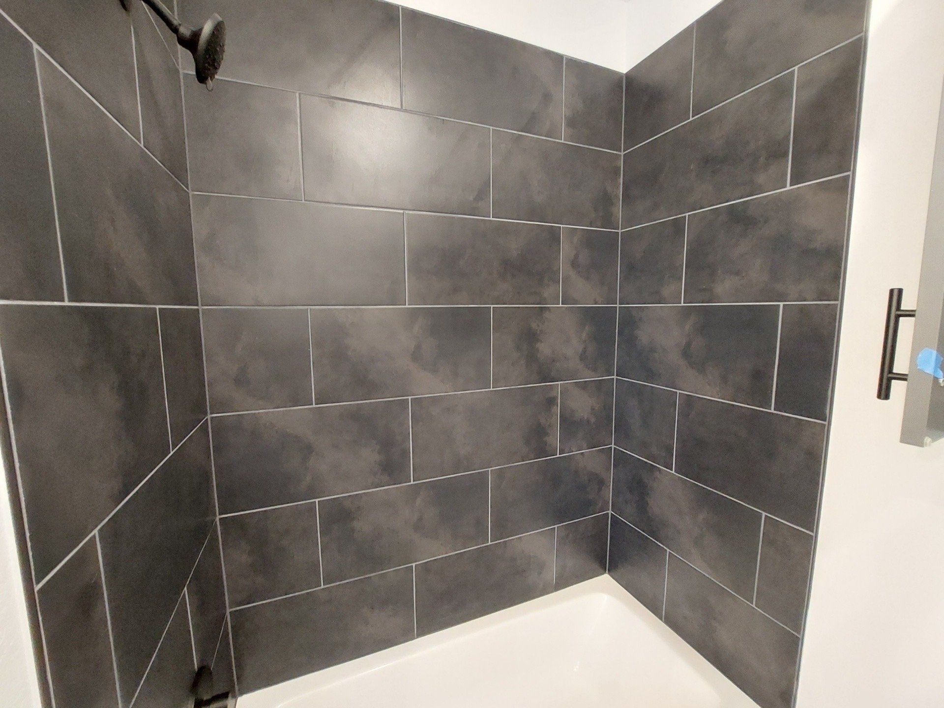 Shower stall with dark gray rectangular tiles and black fixtures.