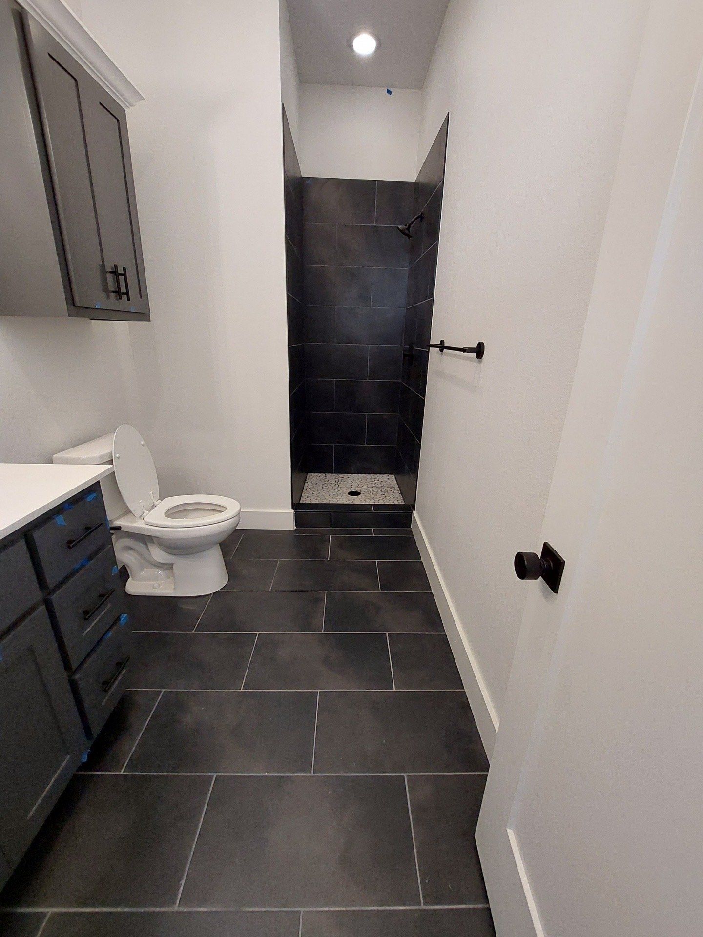 Bathroom with dark tile floor, gray cabinets, white walls, and a black tile shower.