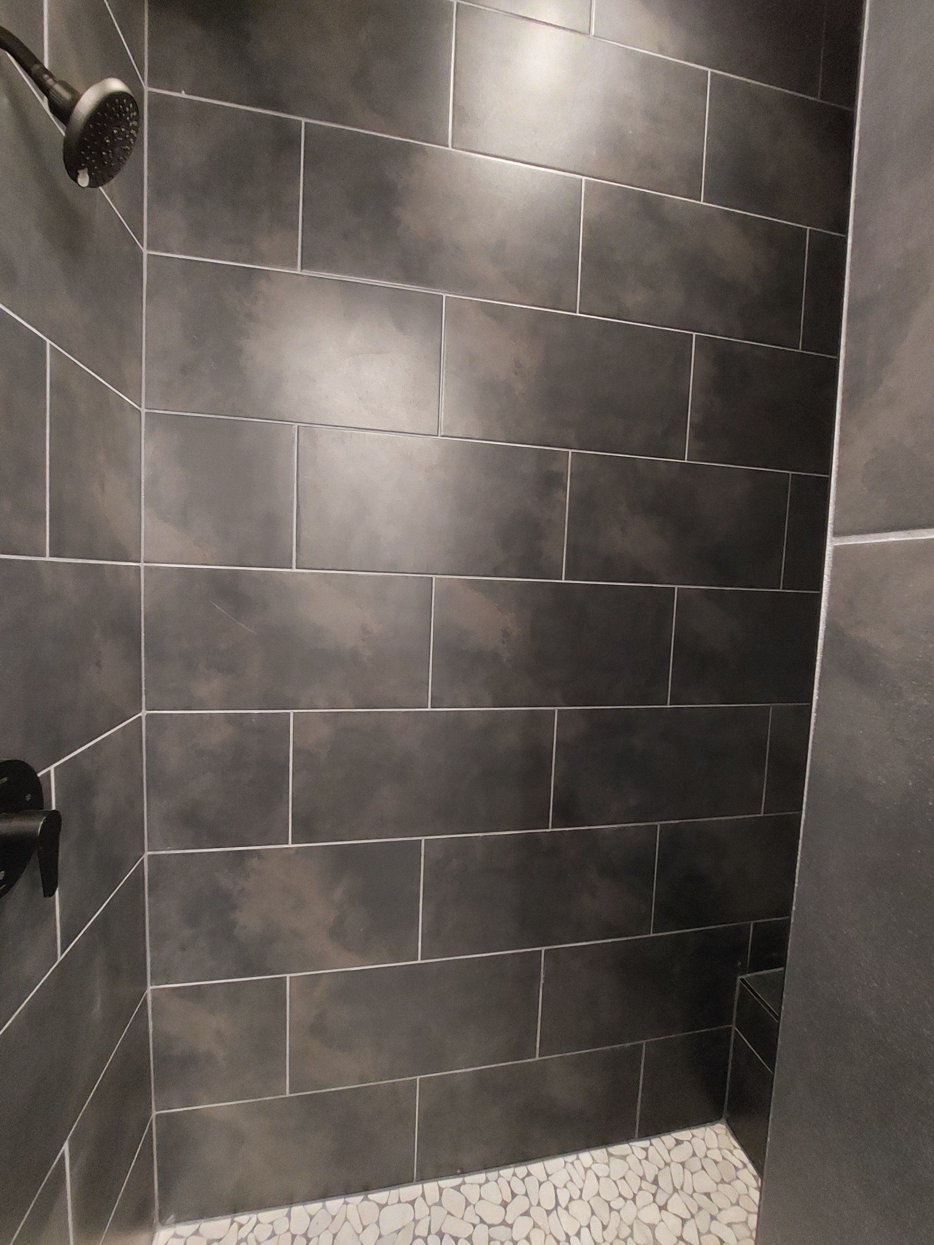Dark gray tiled shower with a black showerhead.