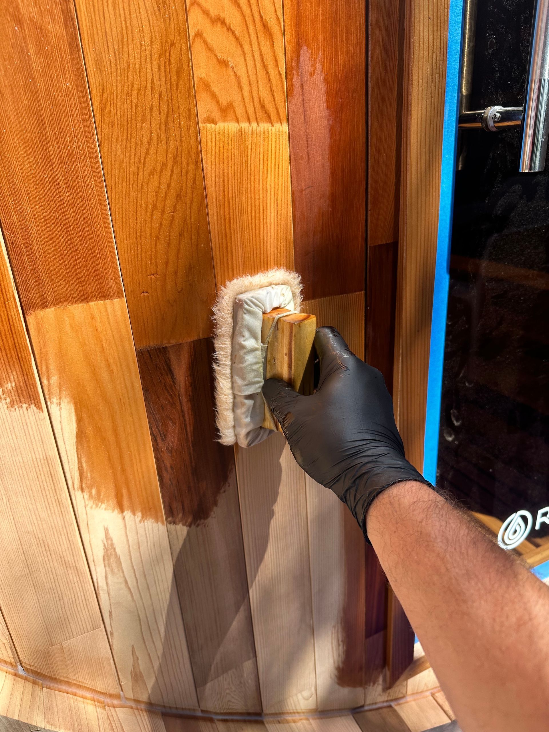 Hand applying stain with a pad to wooden barrel slats, revealing varying shades of wood.