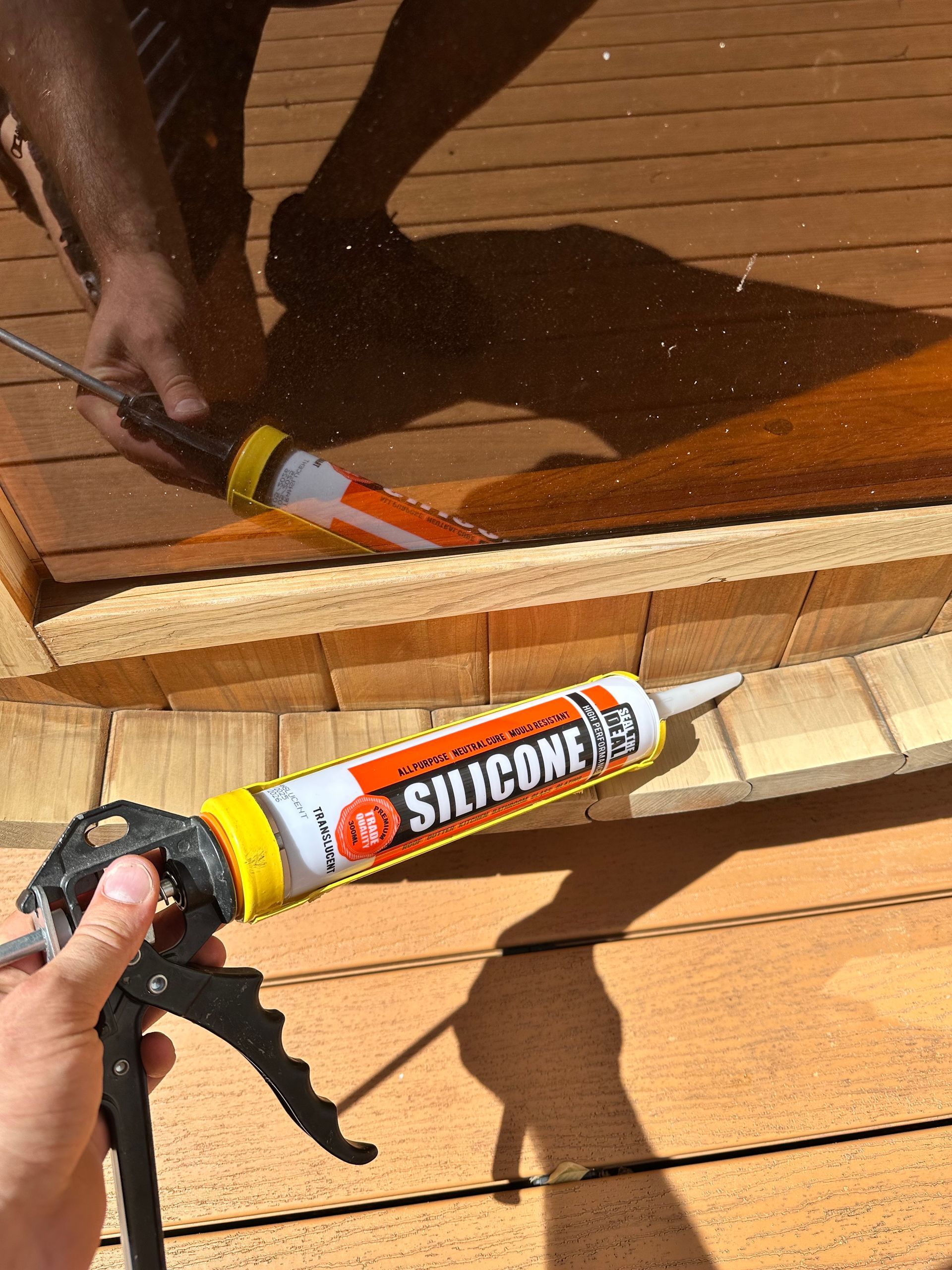 Person applying silicone sealant with a caulk gun to wooden structure.