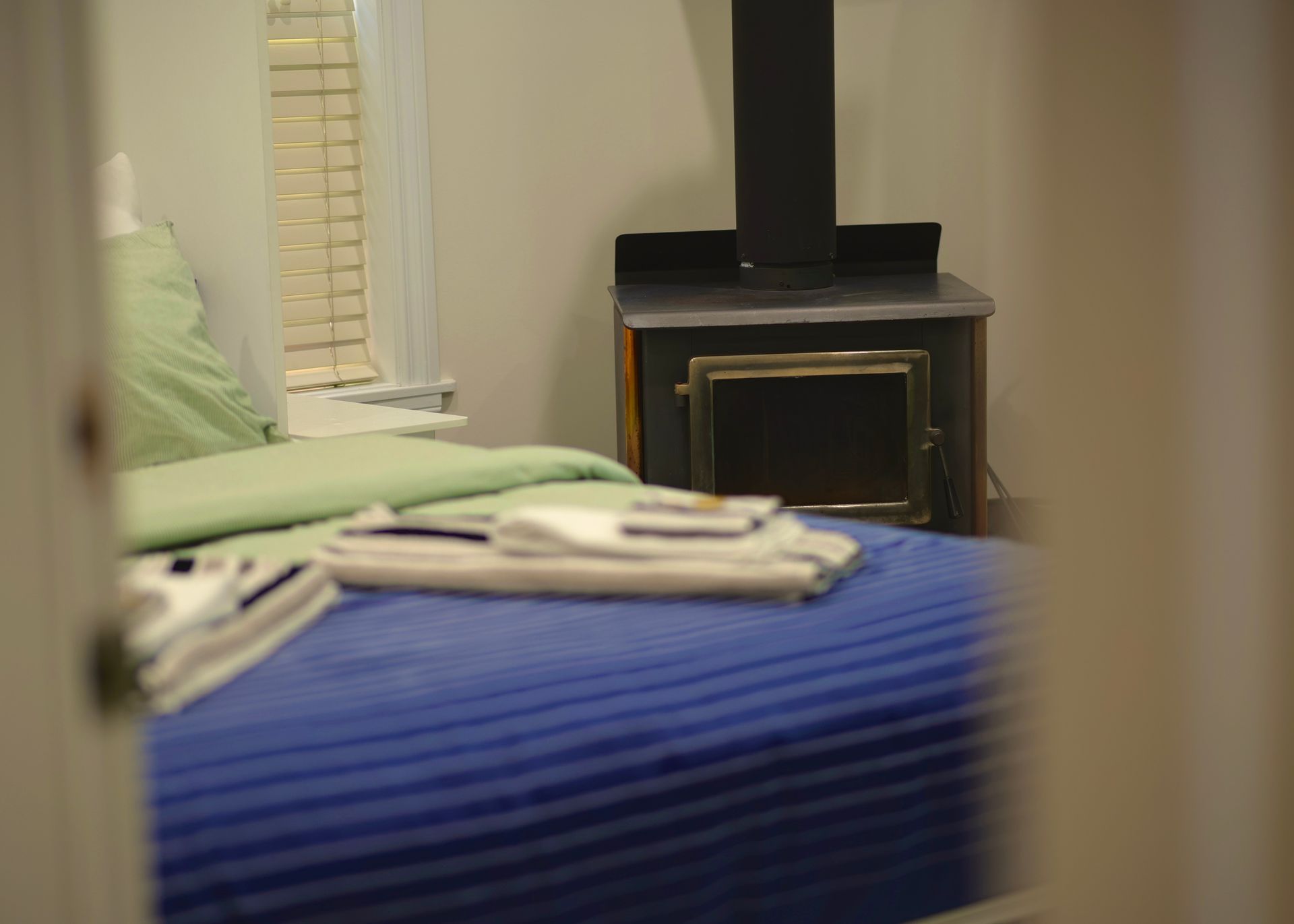 Bedroom with a blue bed, green bedding, and a black stove in a cozy setting.