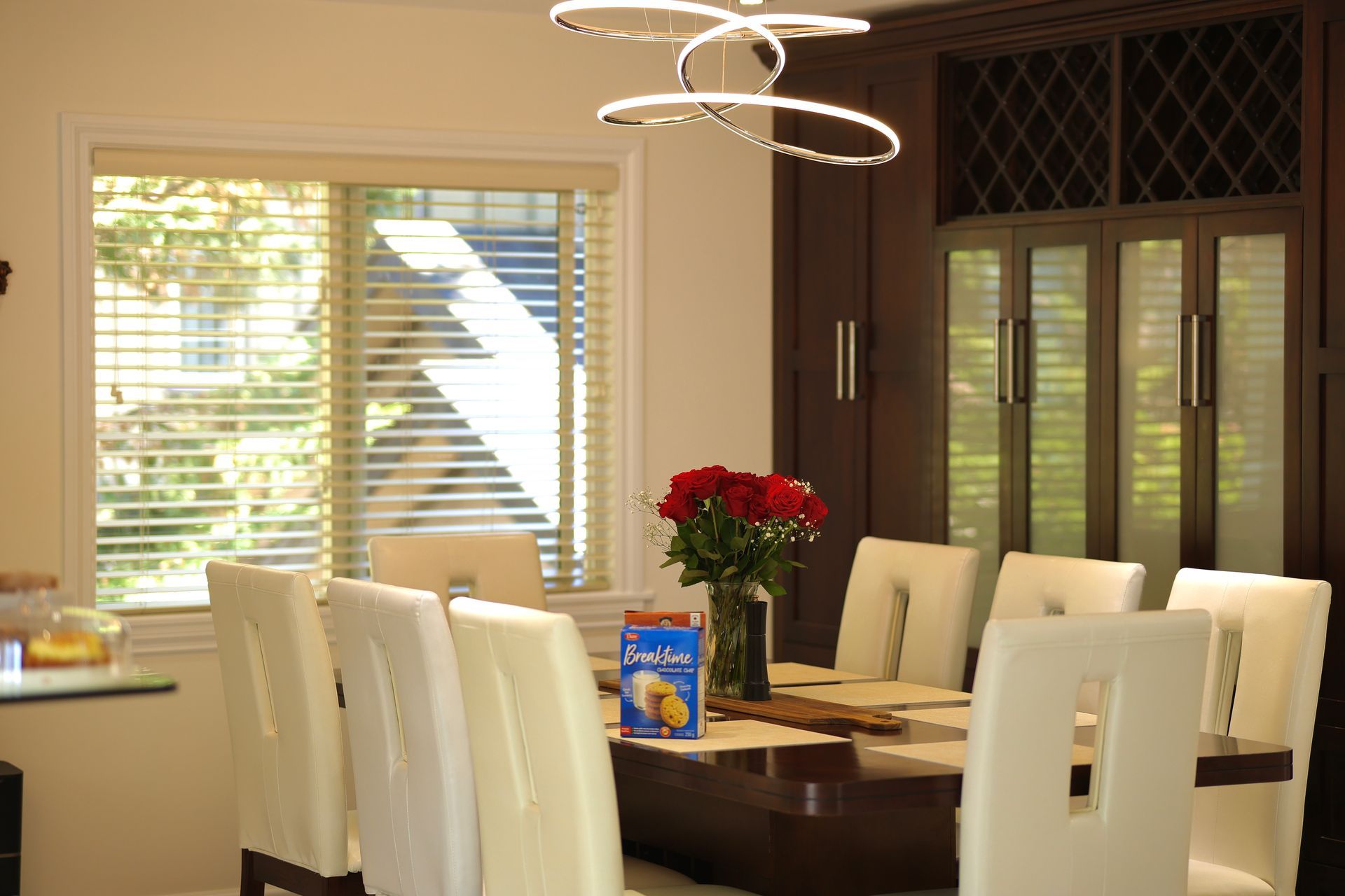 Dining room with a table set for eight, a bouquet of roses, and a large window with blinds.