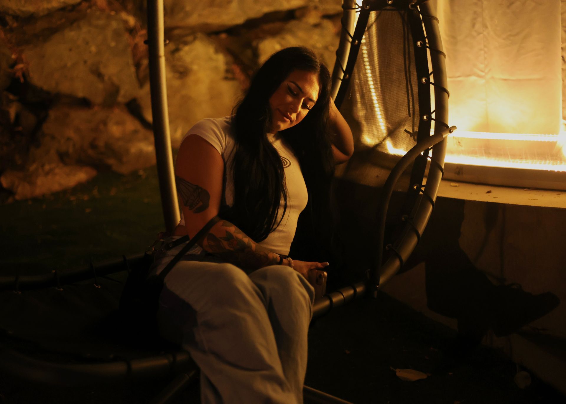 A woman is sitting in a hanging chair with her eyes closed.