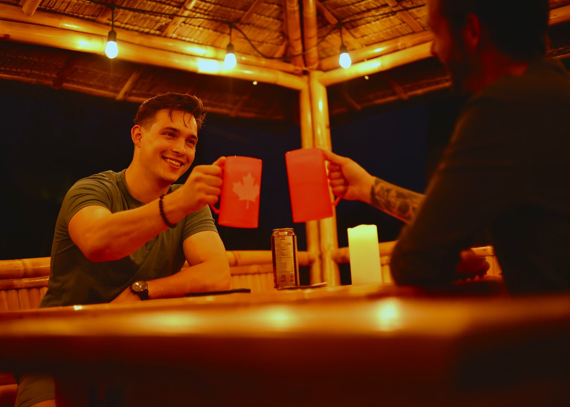 Two men are sitting at a table toasting with cups.