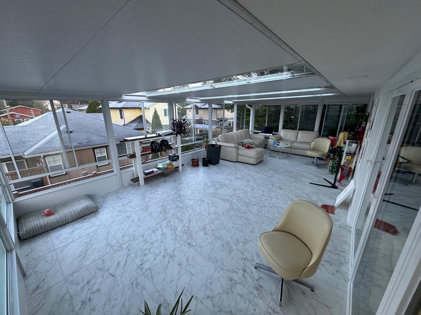 Sunroom with marble floor, white furniture, and glass walls. Exterior view of houses and trees.