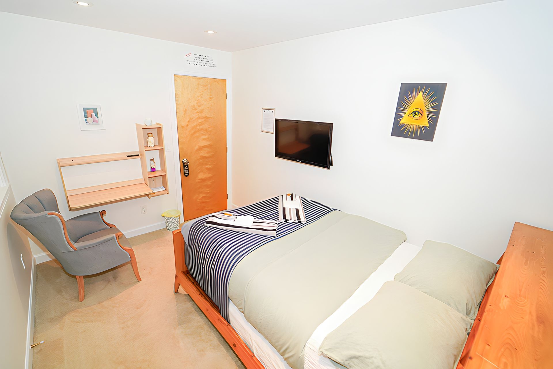 Small bedroom with a bed, desk, chair, TV, and wooden door.