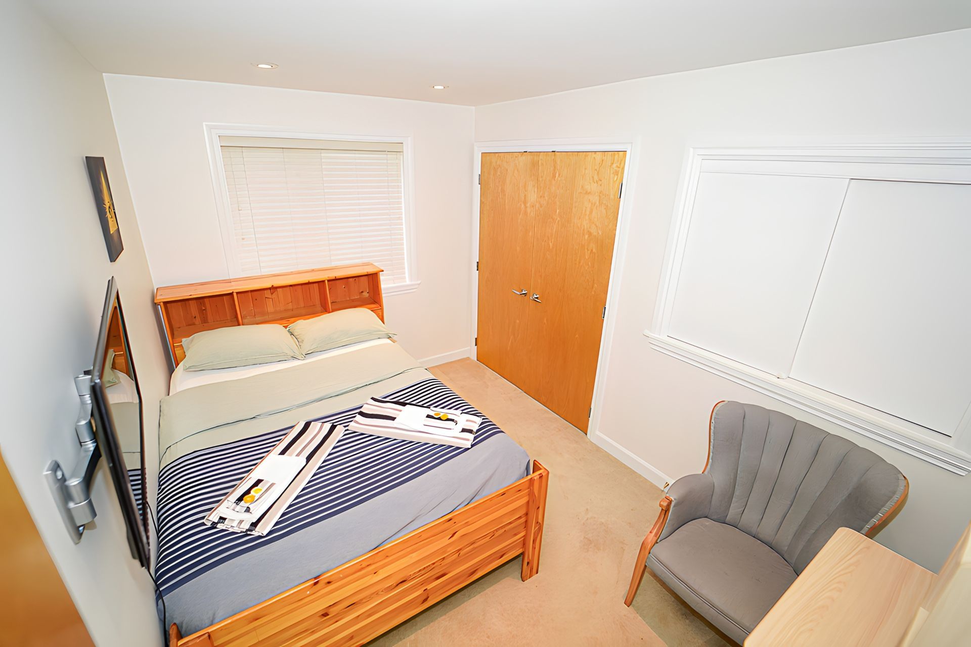Small bedroom with a bed, chair, and closed wooden door. Neutral tones.