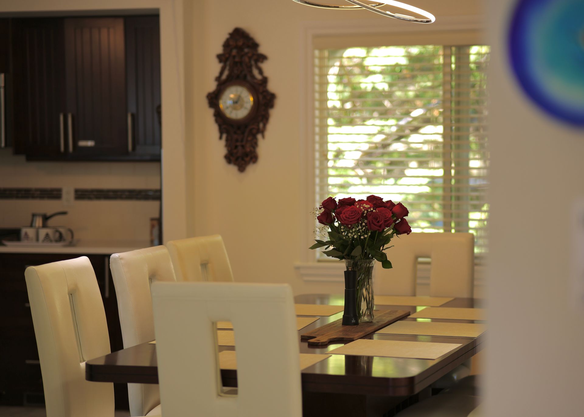 Dining room with table set, chairs, and red flower bouquet; dark cabinets in the background.