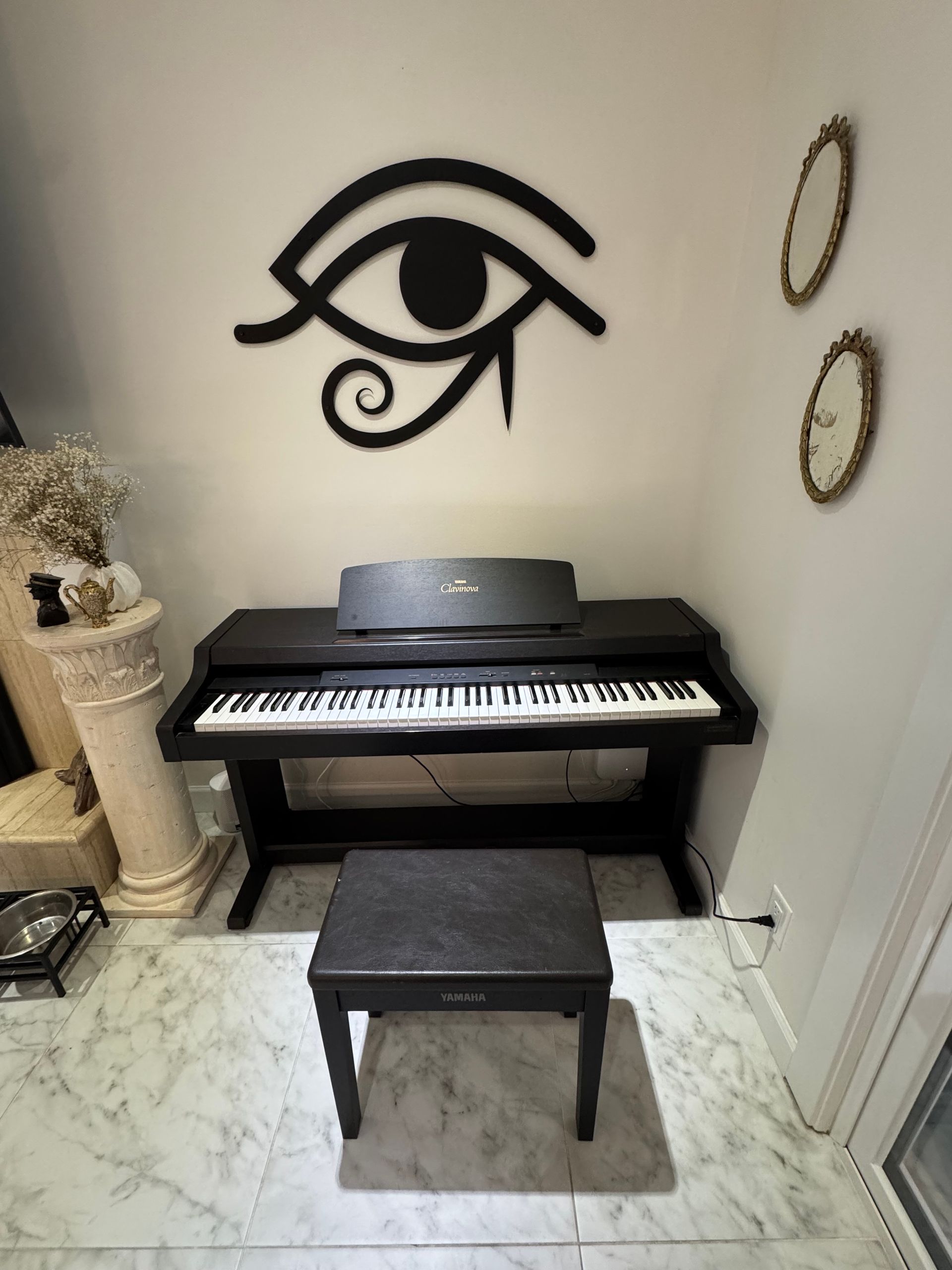 Black piano with stool under a large Eye of Horus symbol on a white wall.