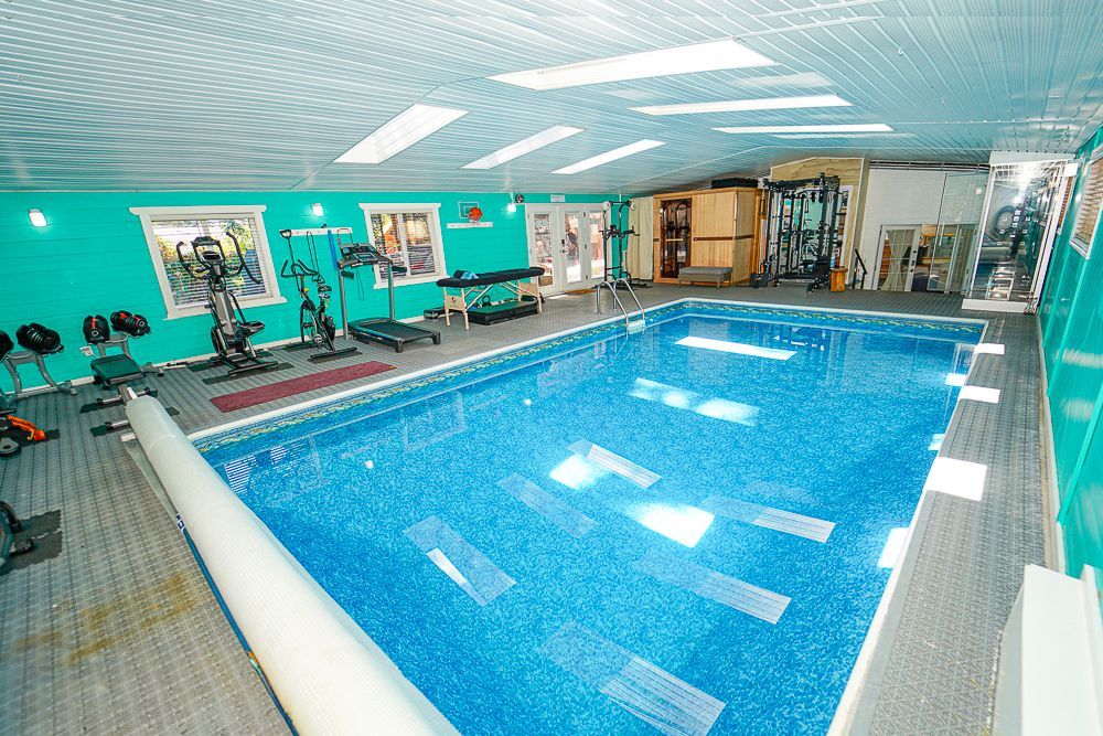 Indoor swimming pool with exercise equipment and a teal wall.