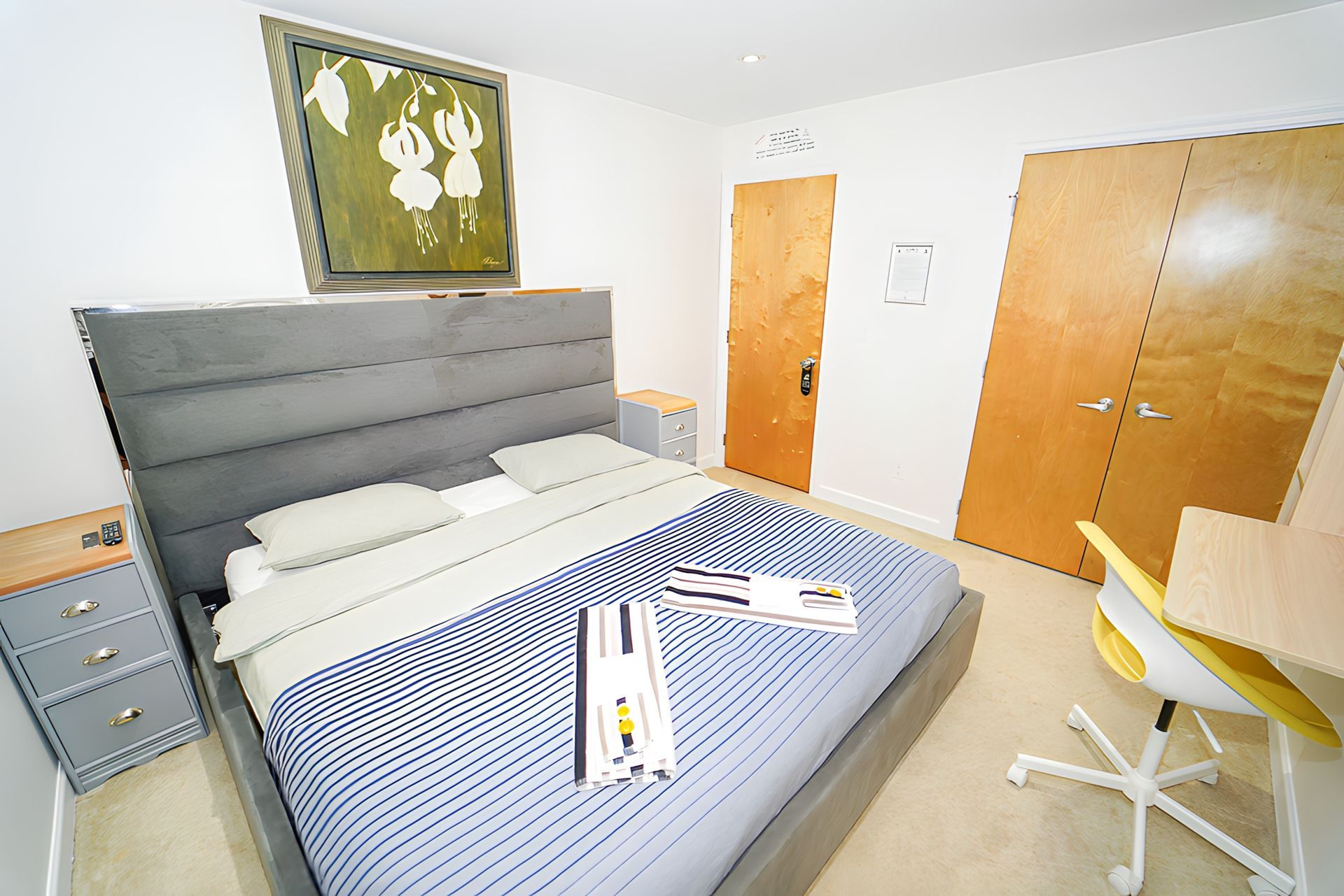 Bedroom with gray bed, artwork, wooden doors, and a yellow desk chair.