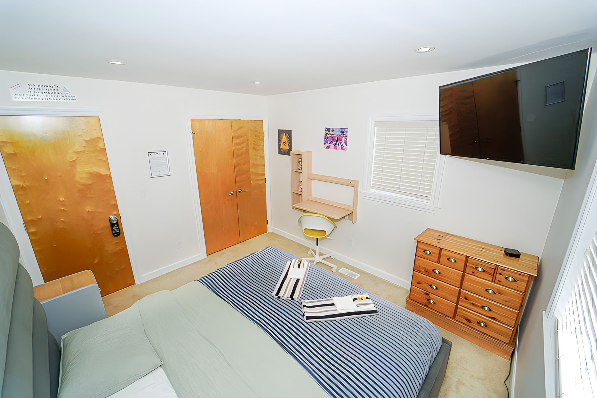 Bedroom with bed, desk, dresser, TV, and door.