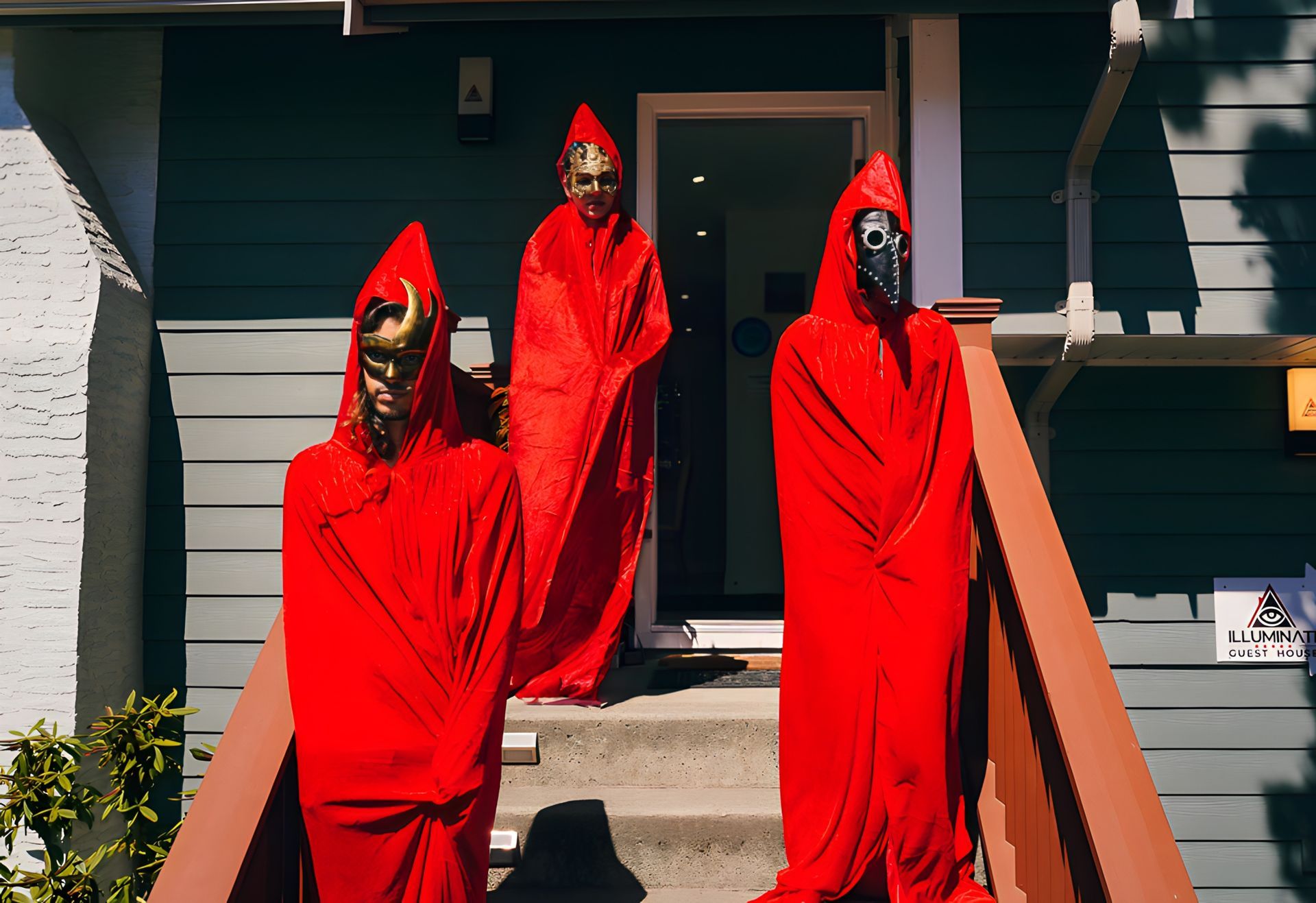 Three people in red cloaks are standing on the steps of a house.