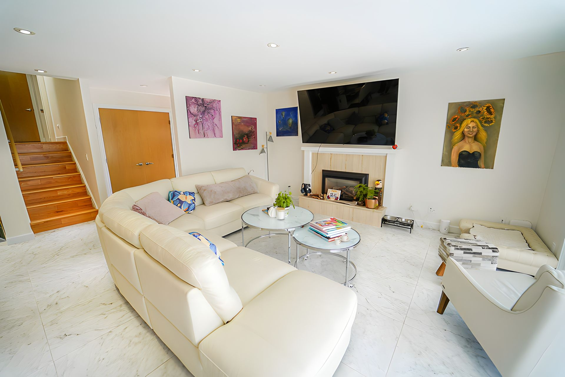 Spacious living room with white walls, leather sofa, fireplace, and artwork.