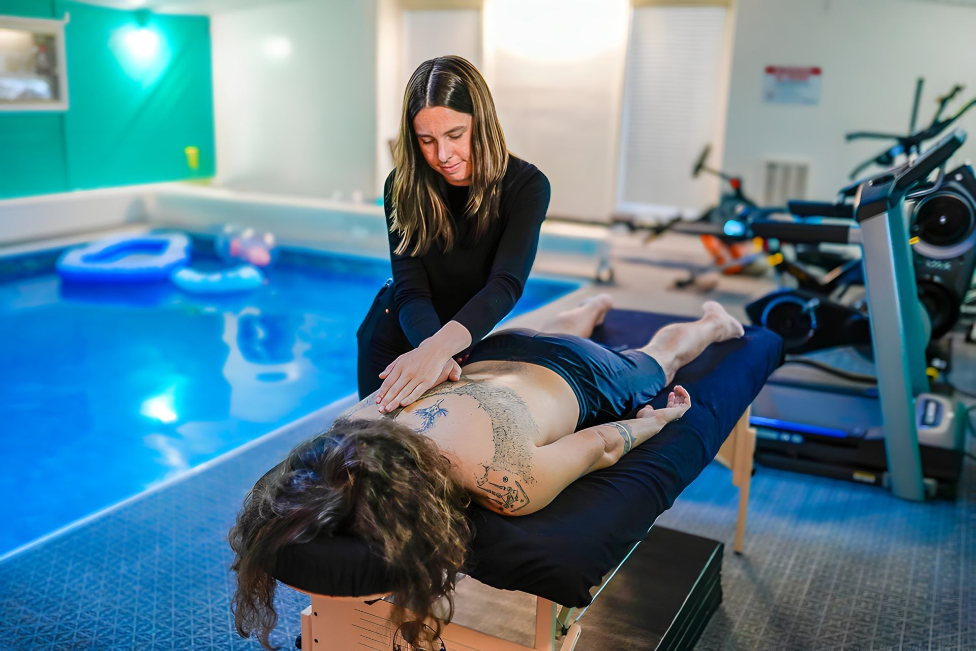 Woman giving a massage on a table near a pool.