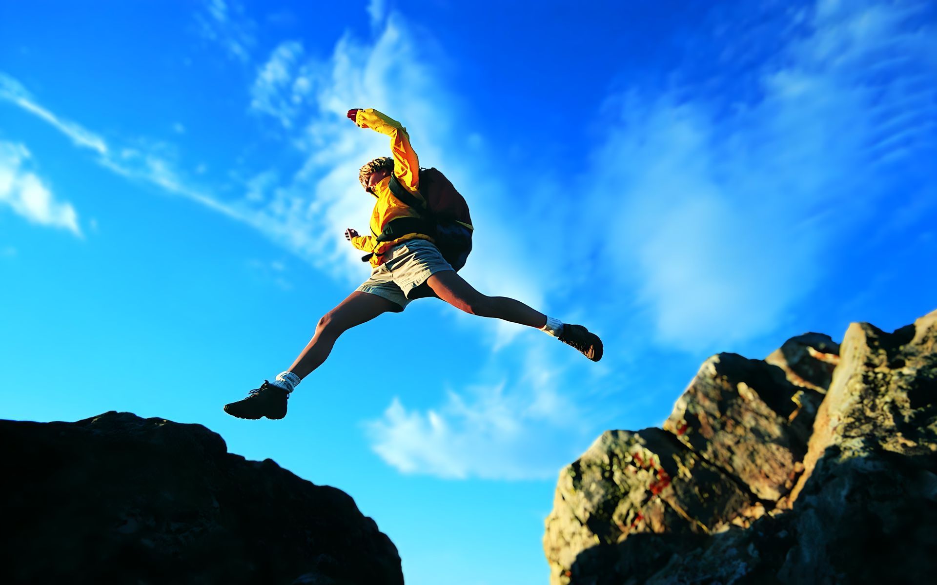 A person with a backpack is jumping over a rocky cliff